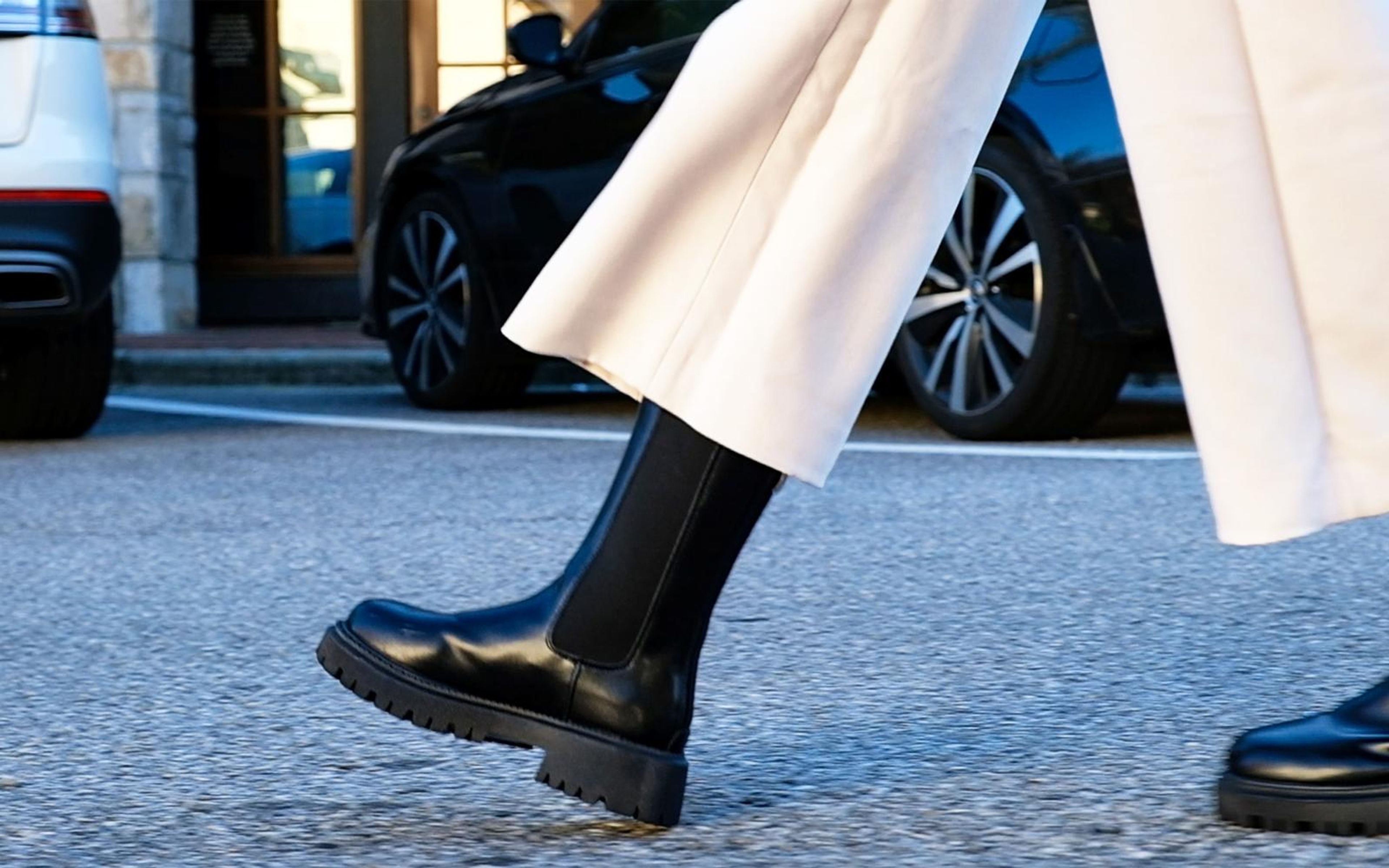 Low close shot of cream wide trousers and black chunky boots stepping across asphalt