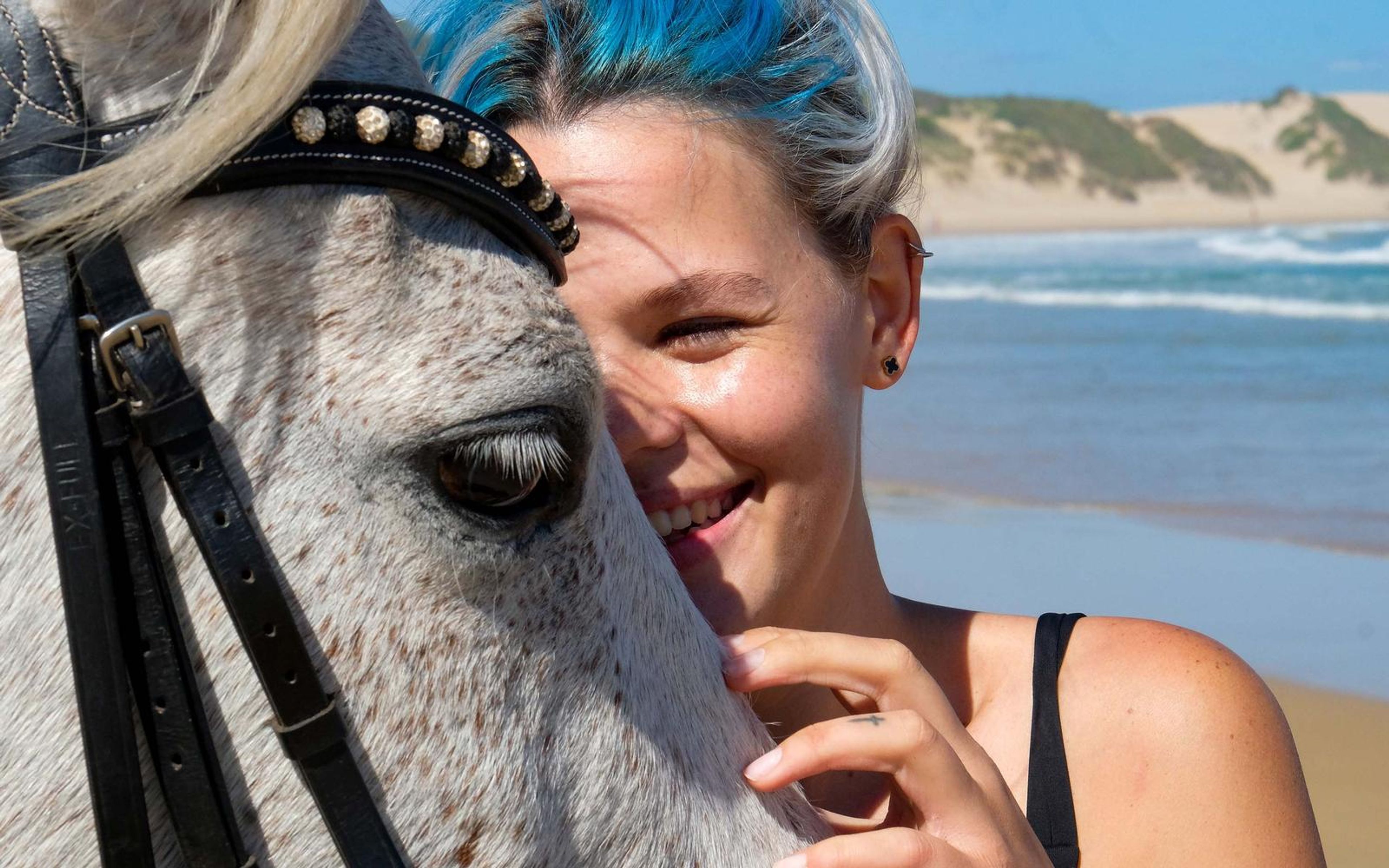 Woman with blue-streaked hair touching a white horse's muzzle, looking up at it, close portrait
