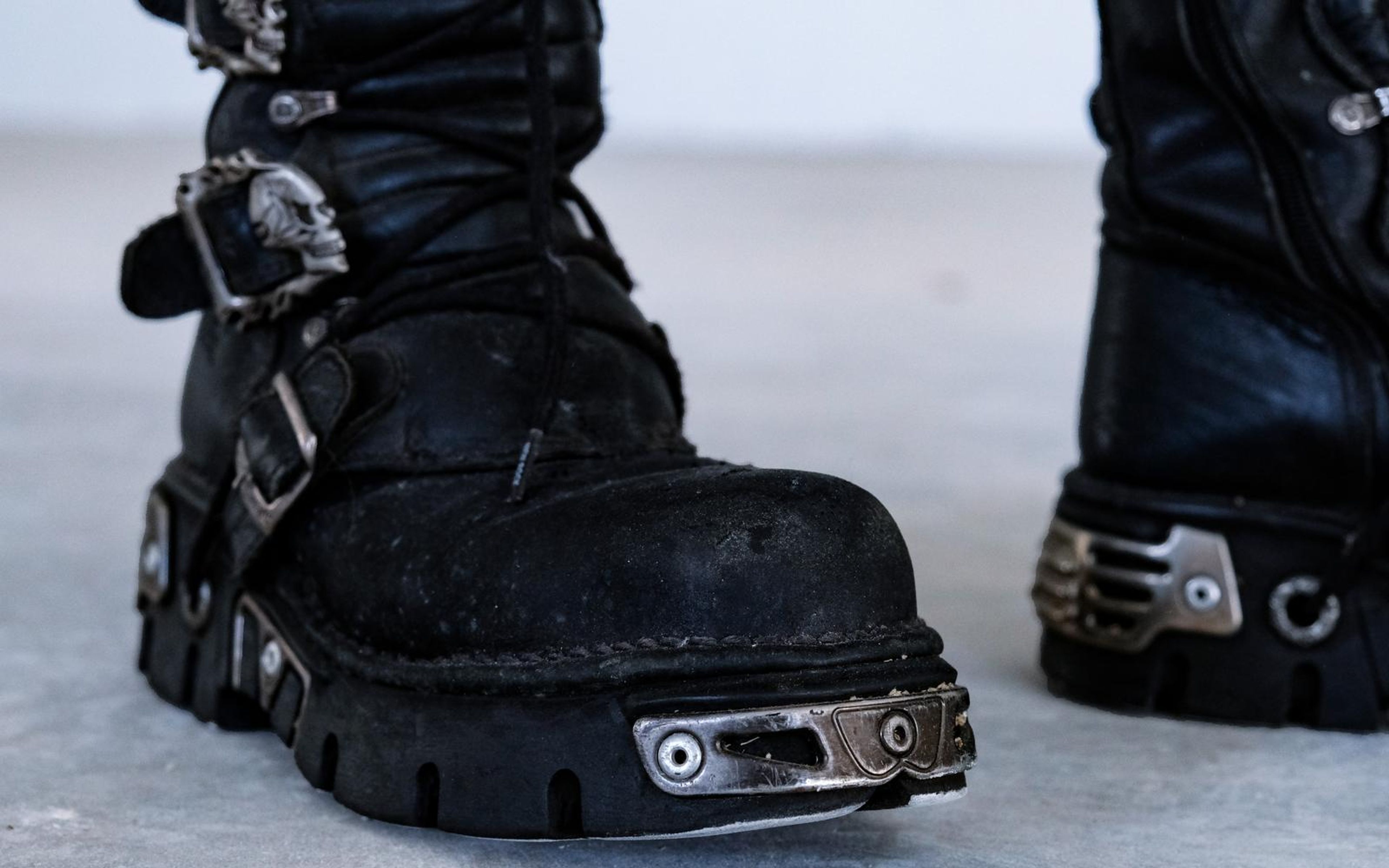 Toe of a black buckled boot with a metal toe plate and skull clasp, shallow depth of field on concrete