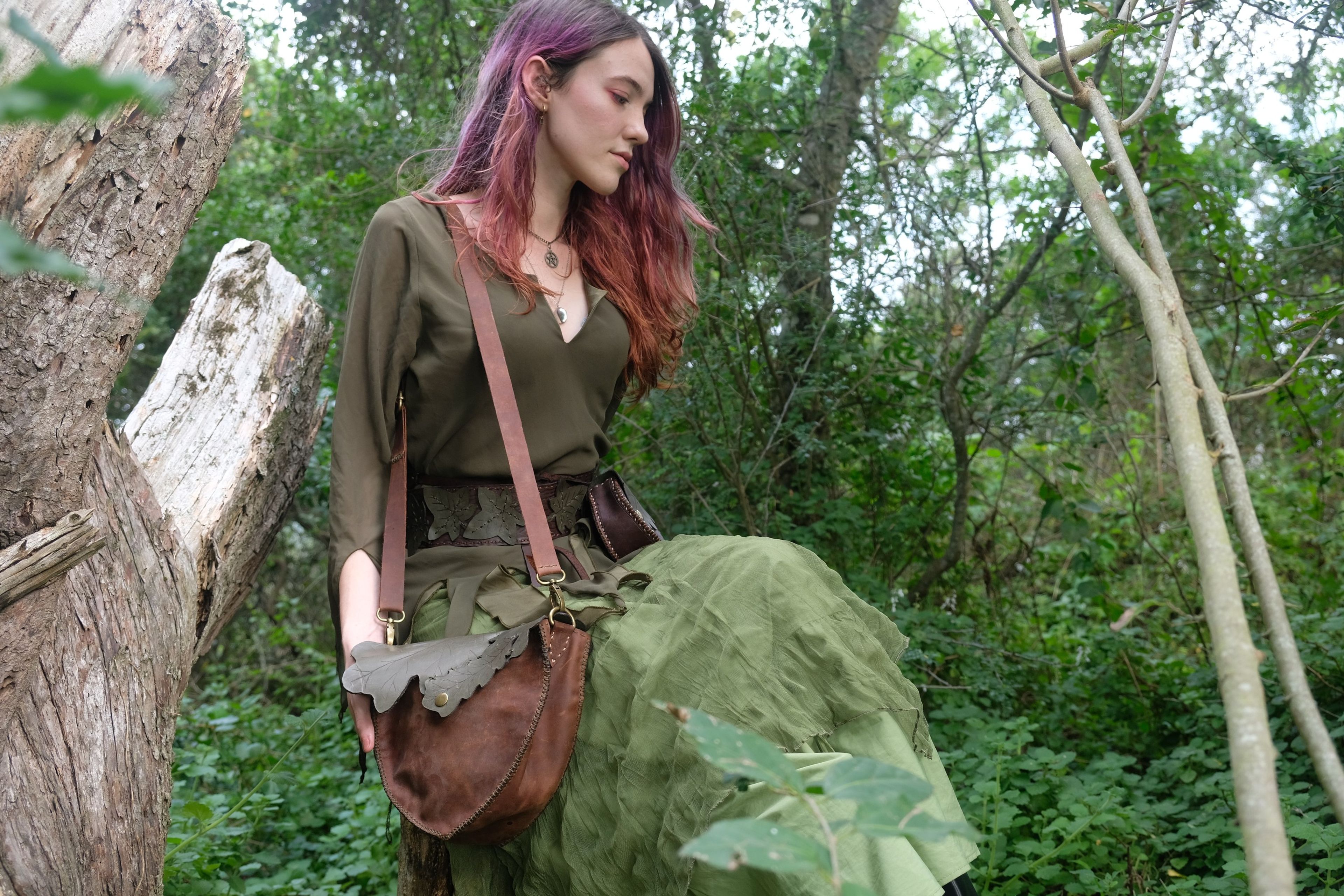 Woman in a green dress seated by a log with a leather bag in her lap