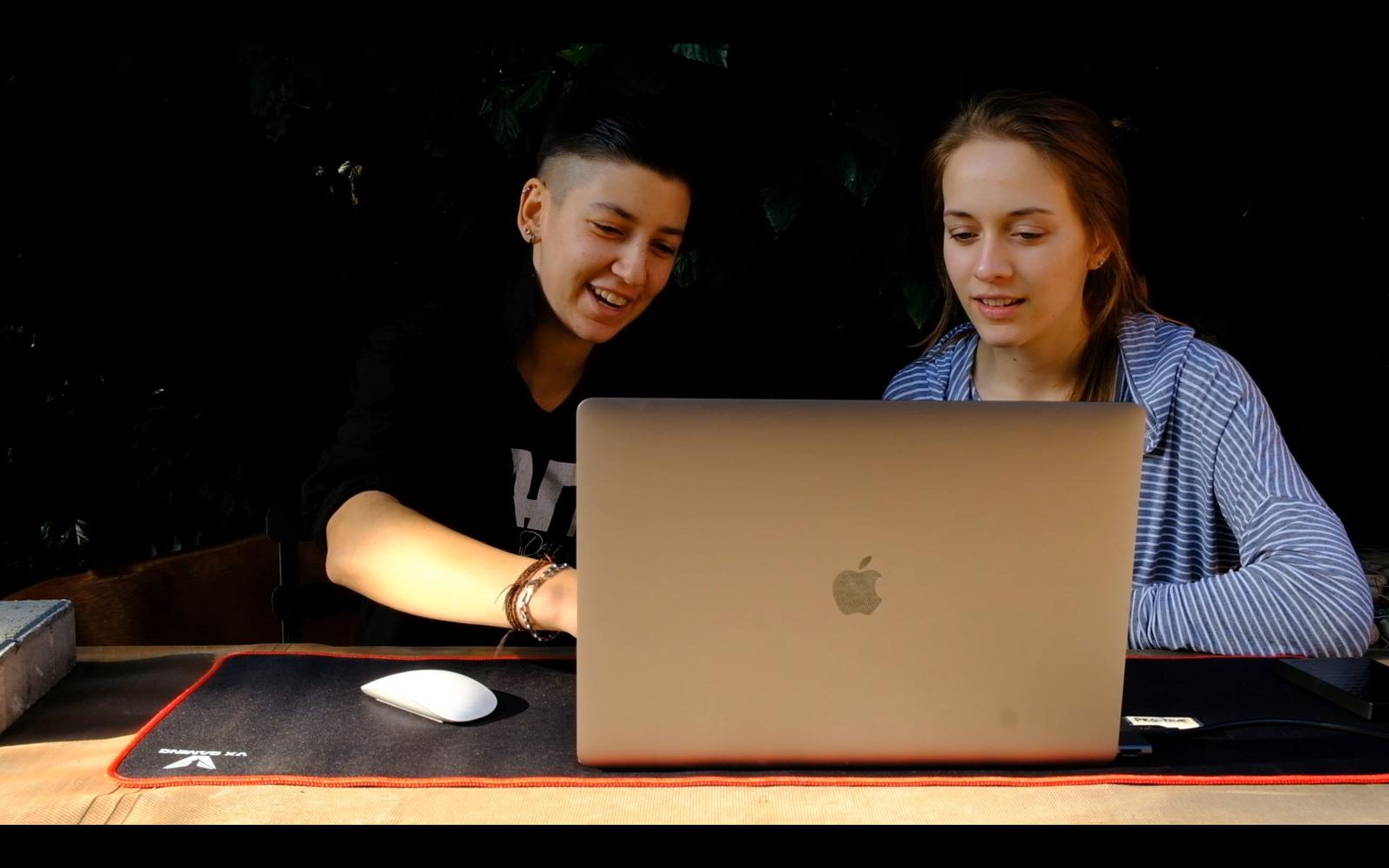 Two people seated at a laptop at a desk reviewing material, one smiling