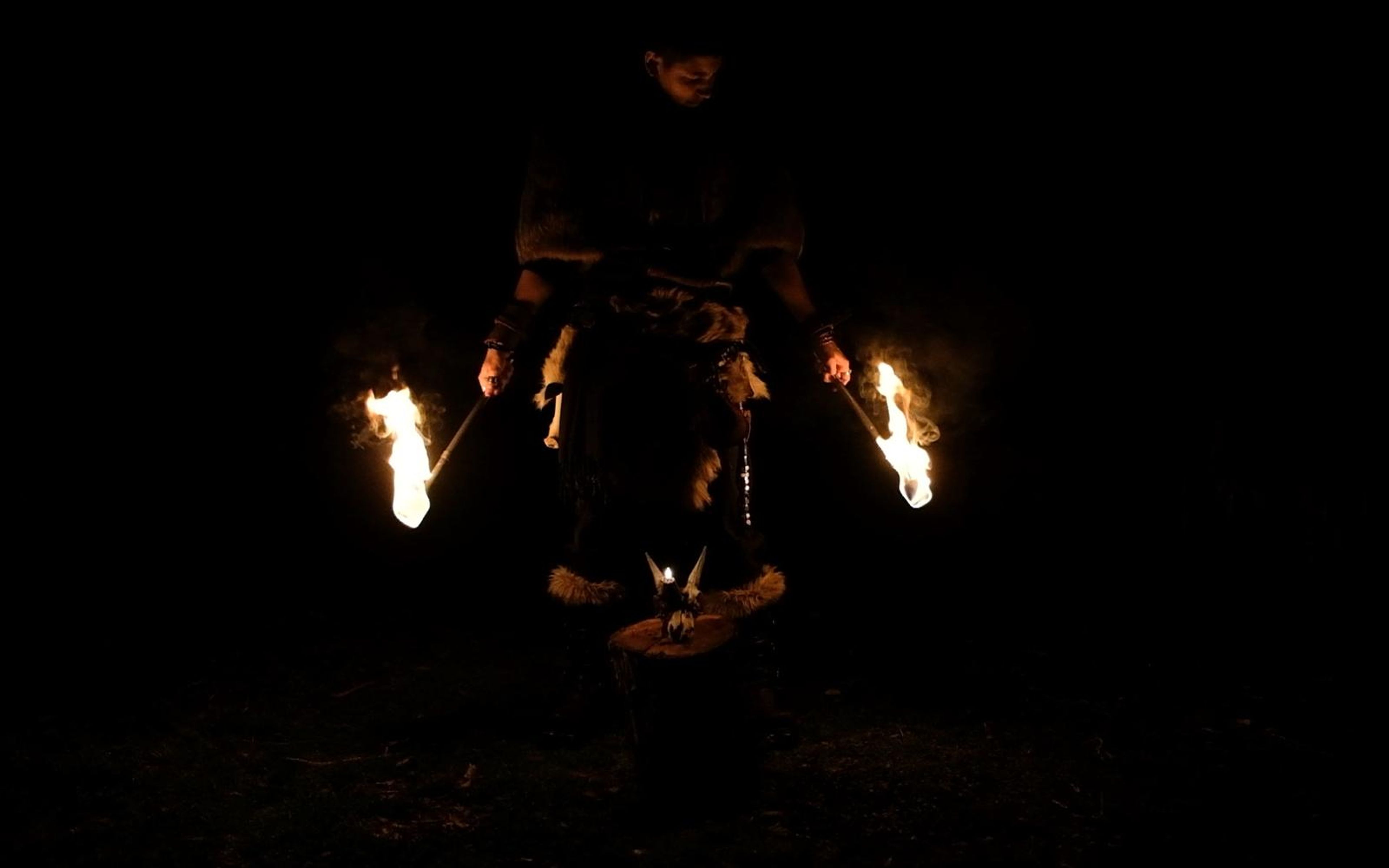 Barbarian standing with a torch flame at each side, a small fire on a stump in front