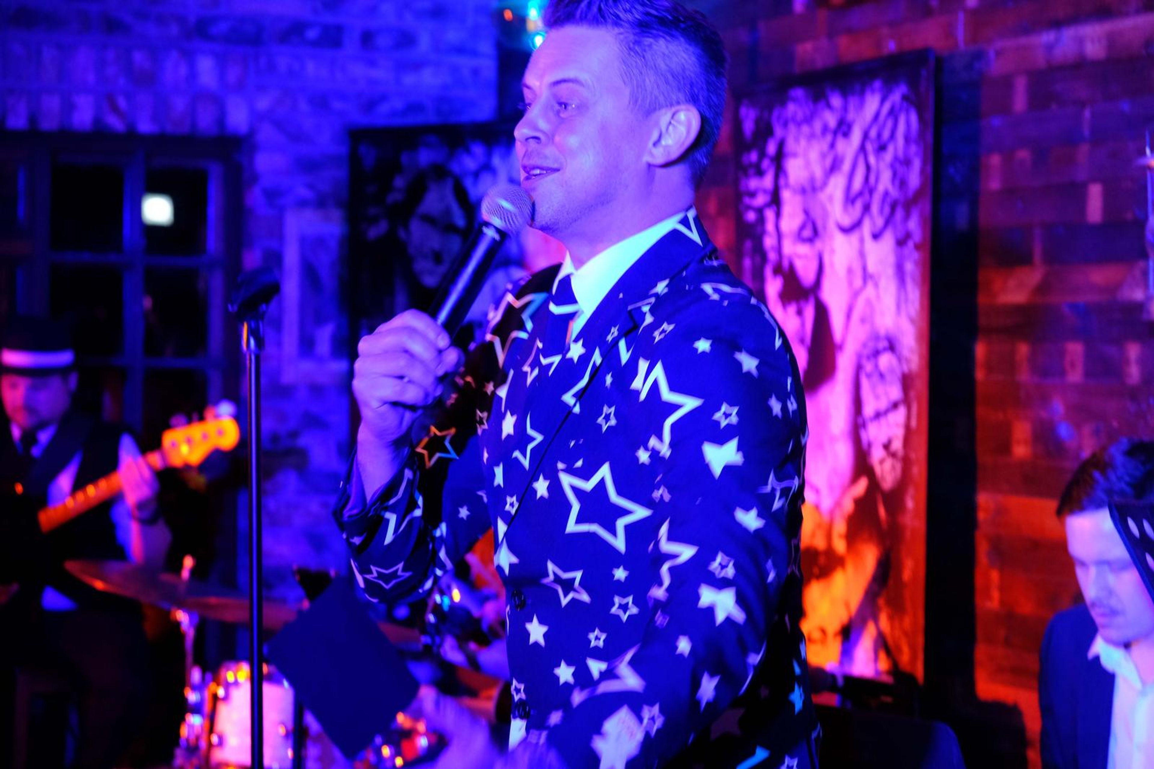 Singer in a star-patterned suit singing to the room