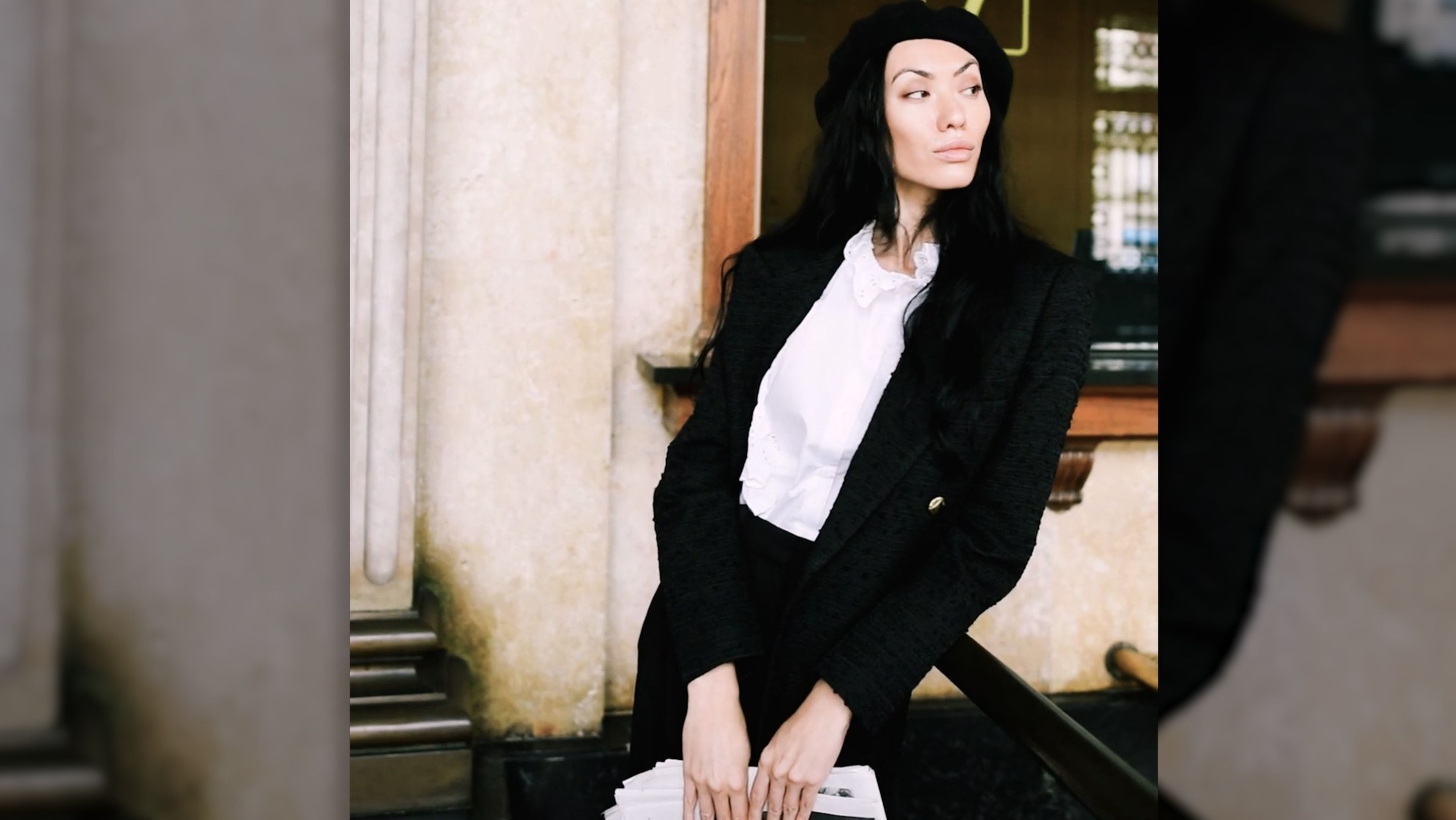 Woman in a black blazer and white shirt seated against a classical stone doorway