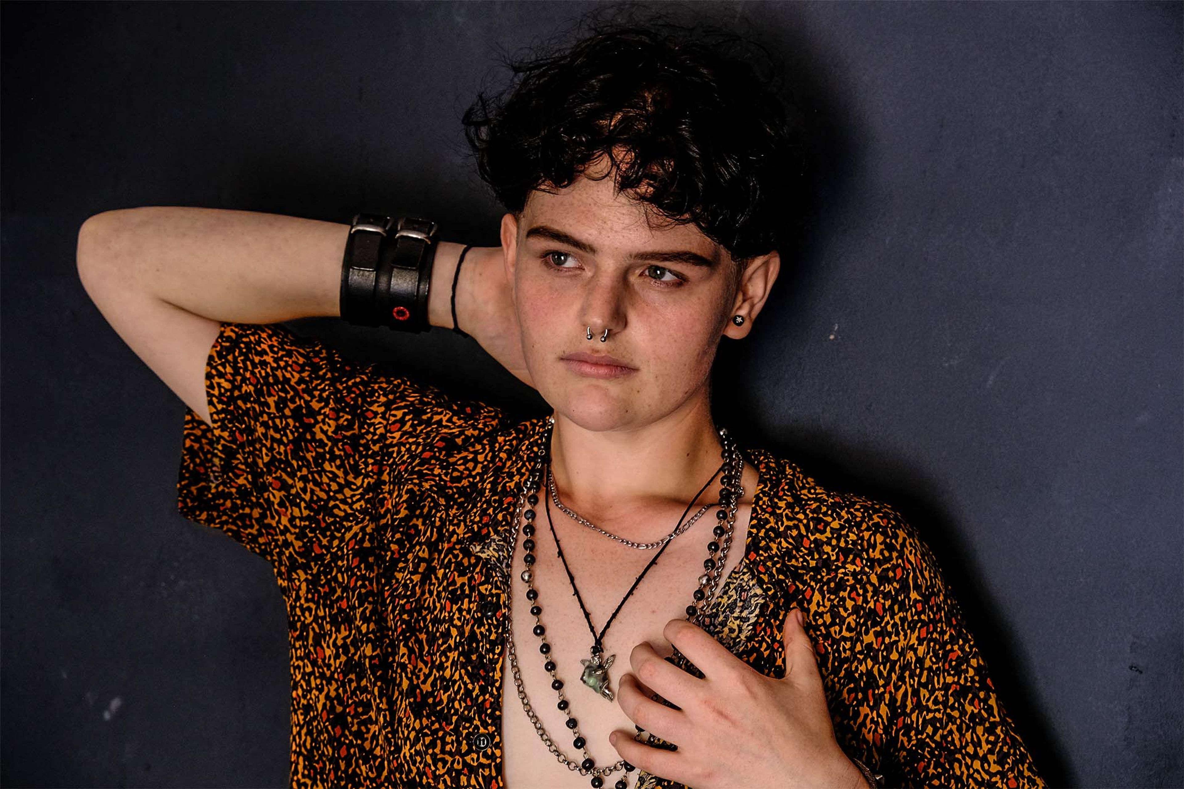 Portrait, subject in a patterned shirt with hand raised to the hair, leather wrist cuff visible