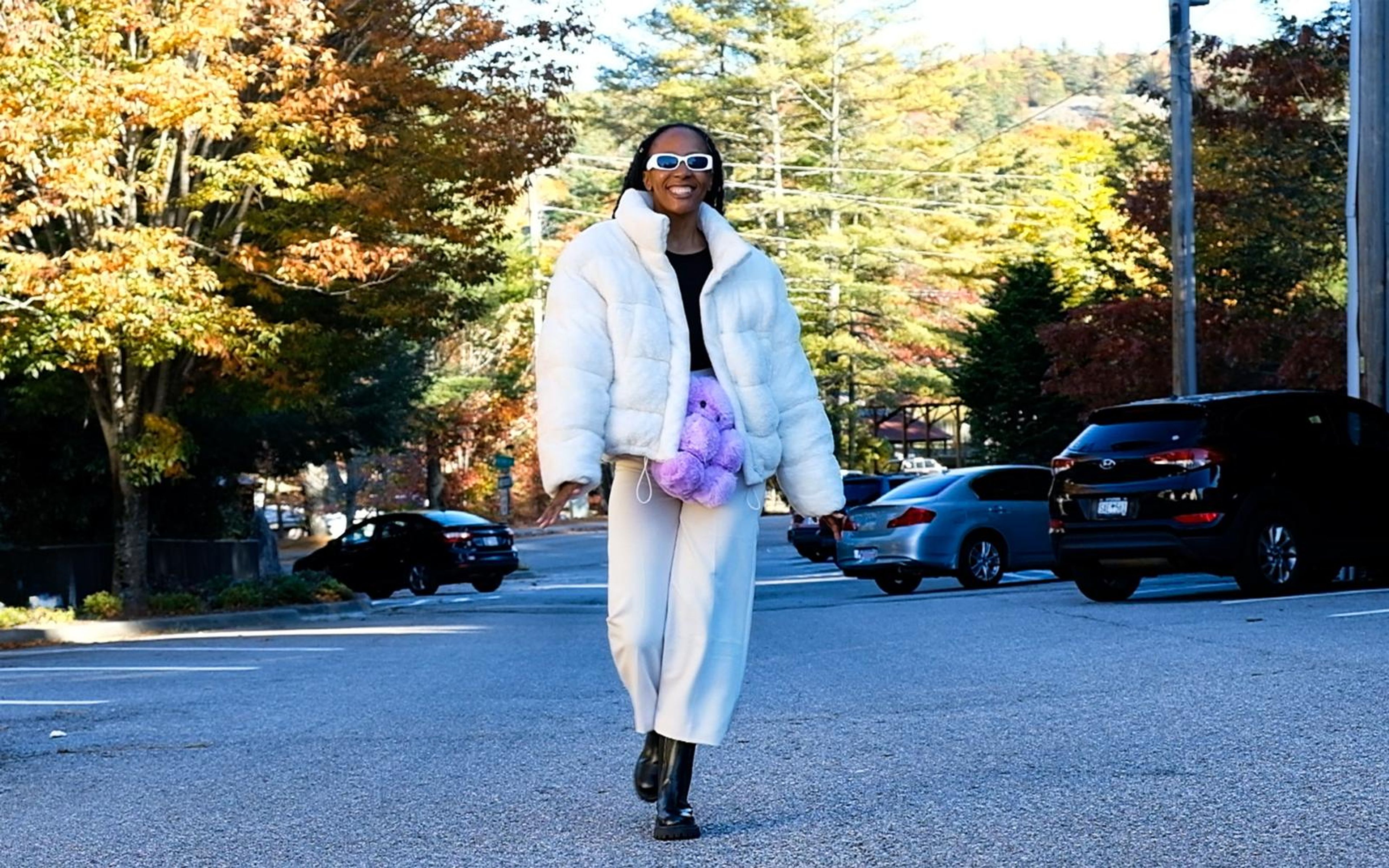 Model walking toward camera on an autumn street in a white fur jacket, cream trousers and black boots