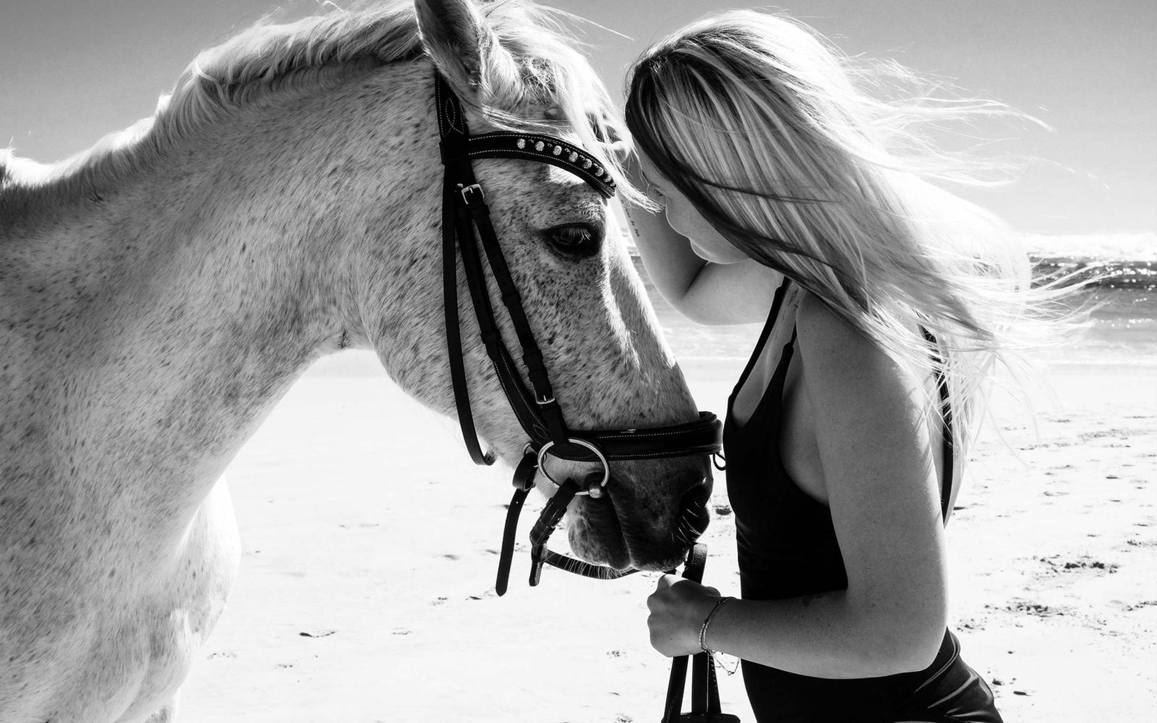 Black and white profile of a woman holding the reins while resting against a white horse, windblown hair
