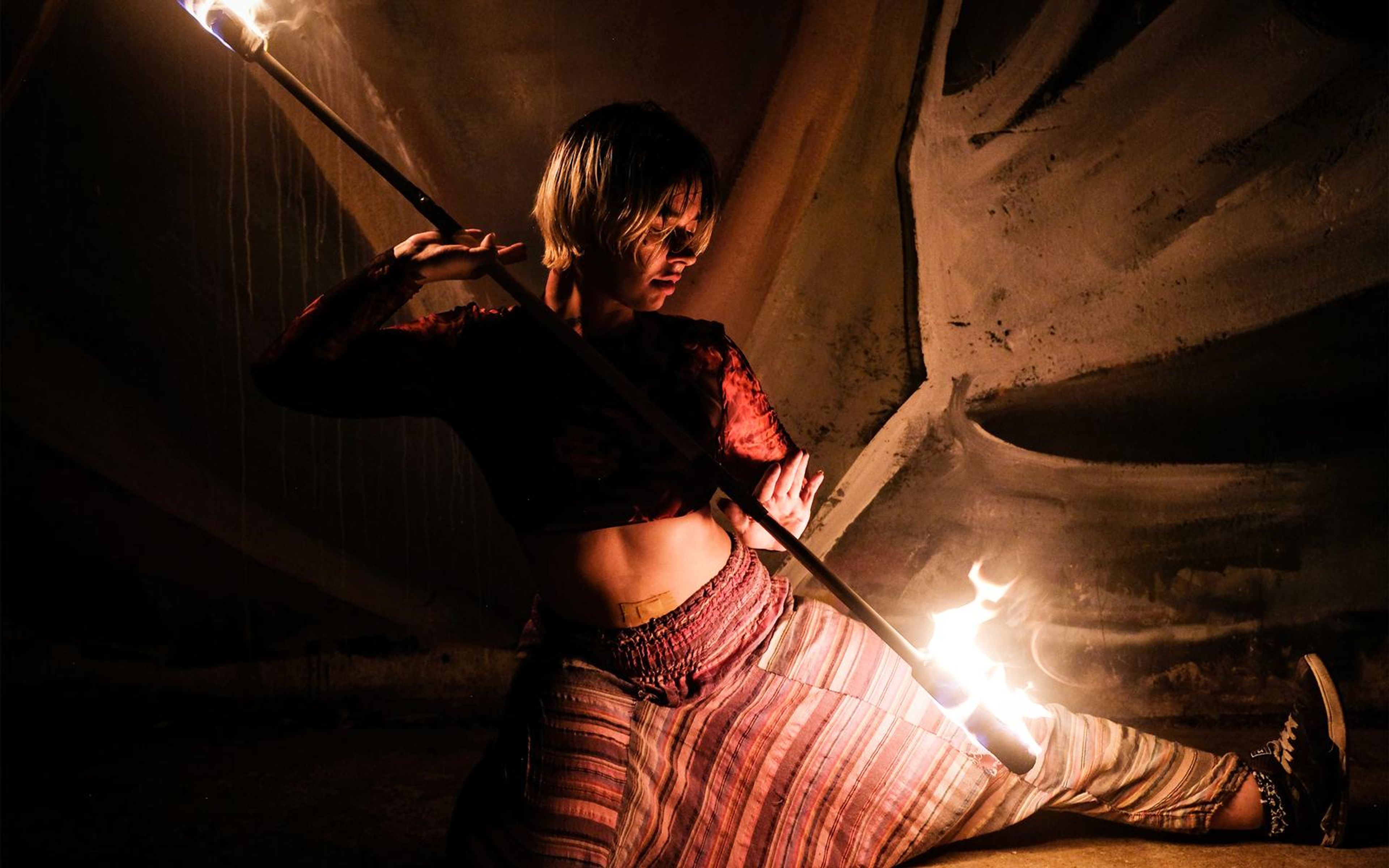 Performer sitting in a side split with a fire staff across the body and a flame near the right foot