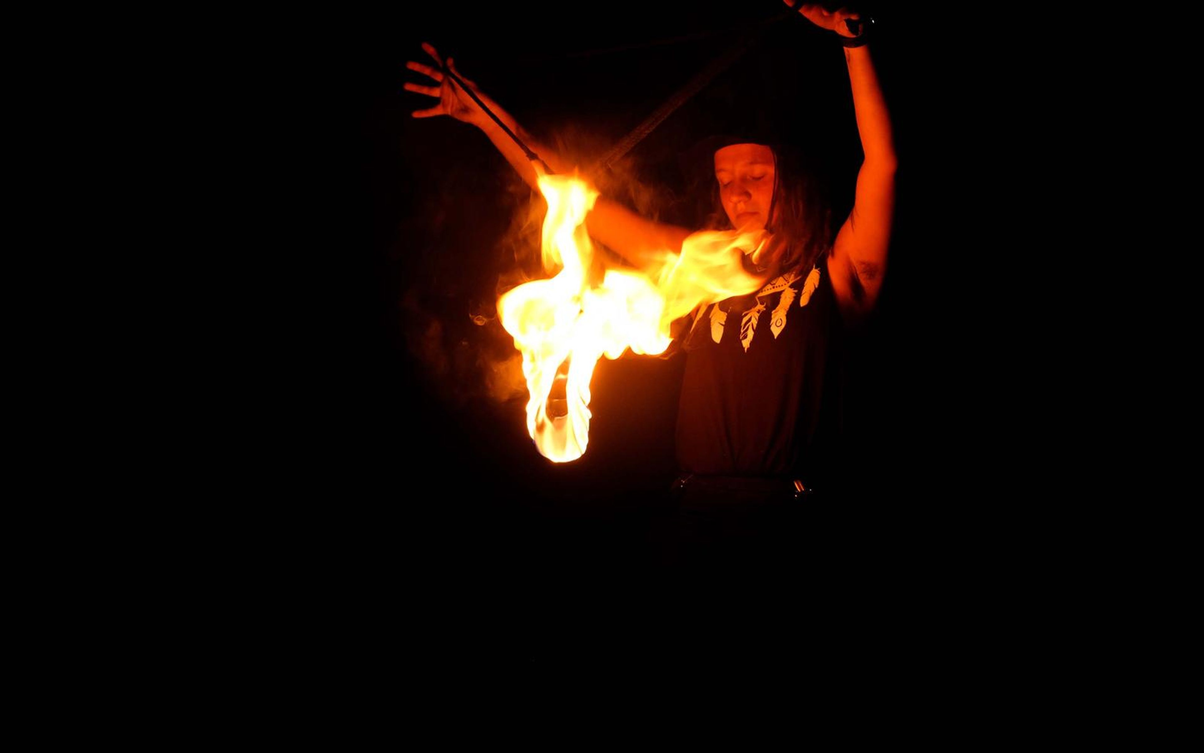 Flame burning at the left of the performer as her hands reach upward, soft smoke around