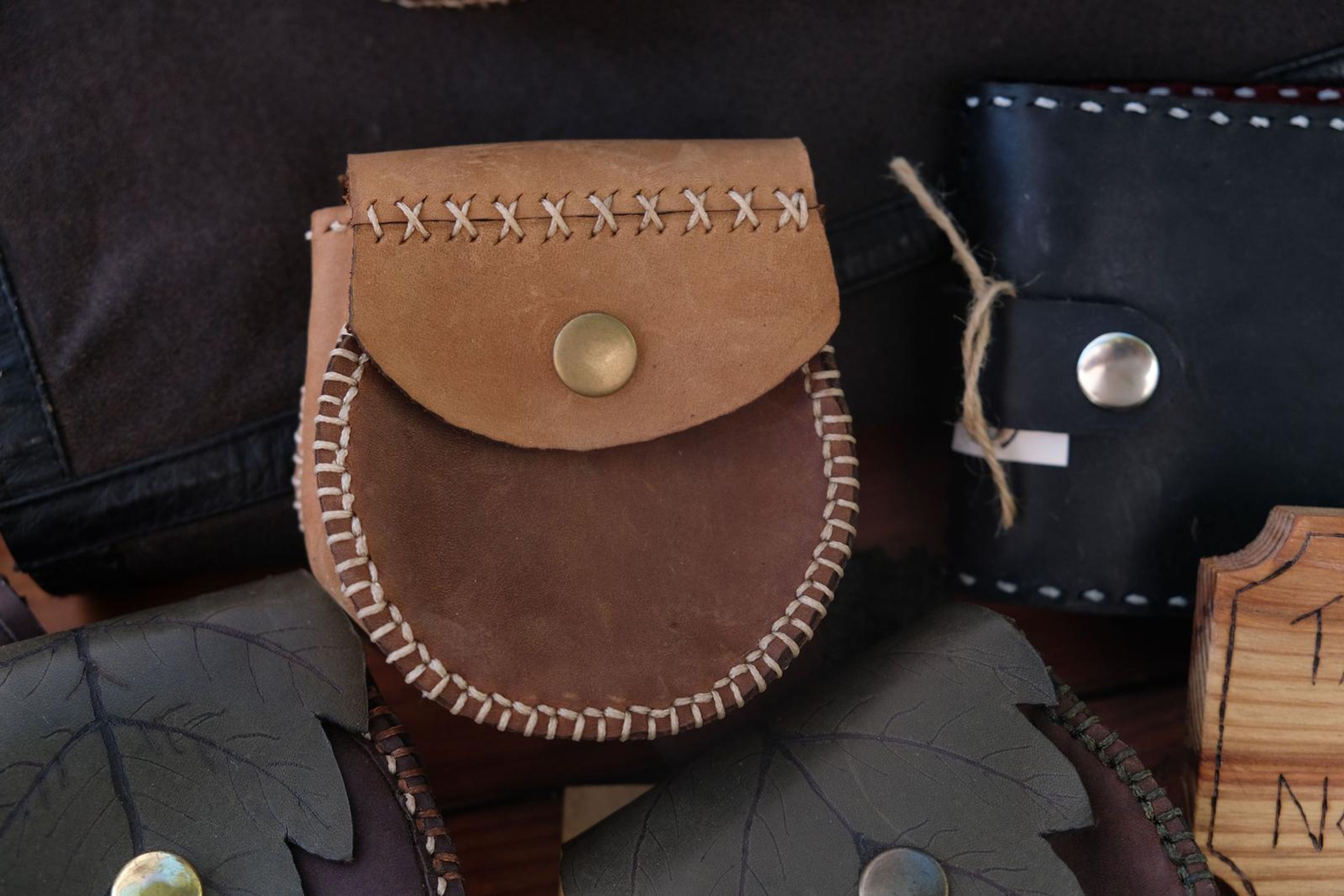 Tan leather pouch with a cross-stitched flap and brass snap beside a black wallet