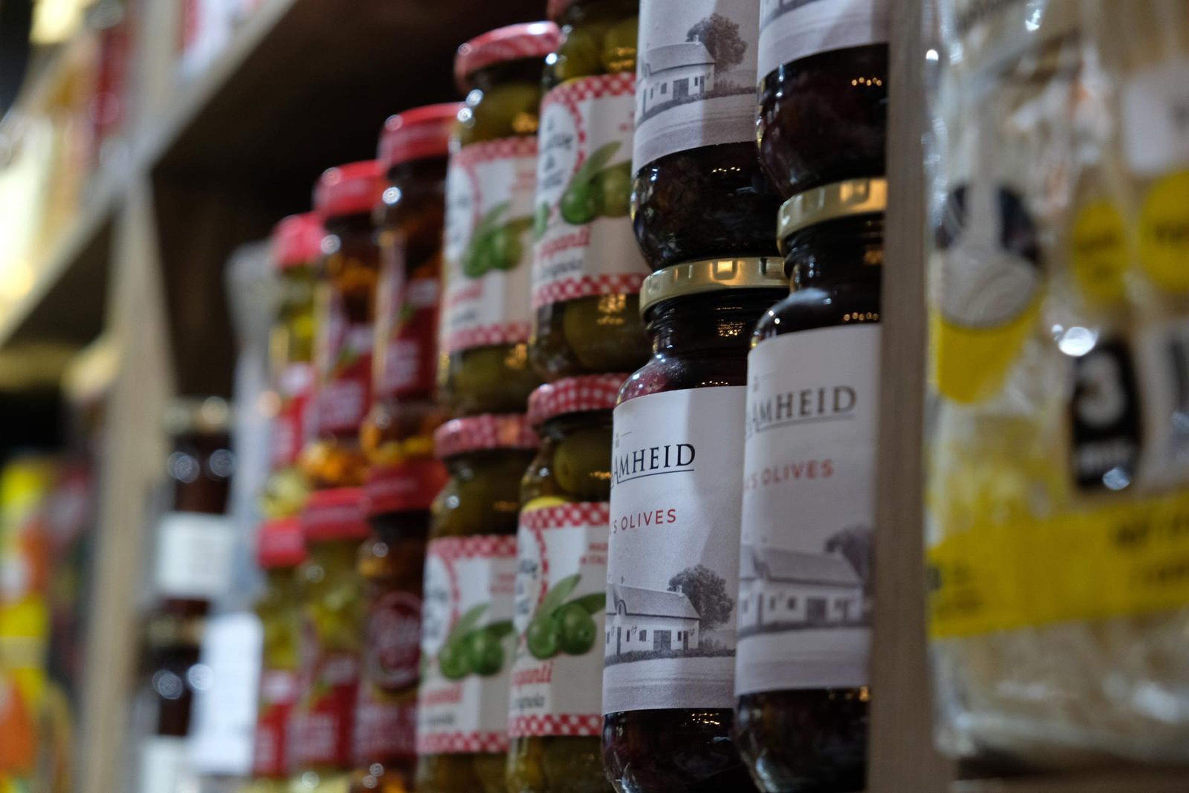Rows of preserved olives and jars on a wooden shelf