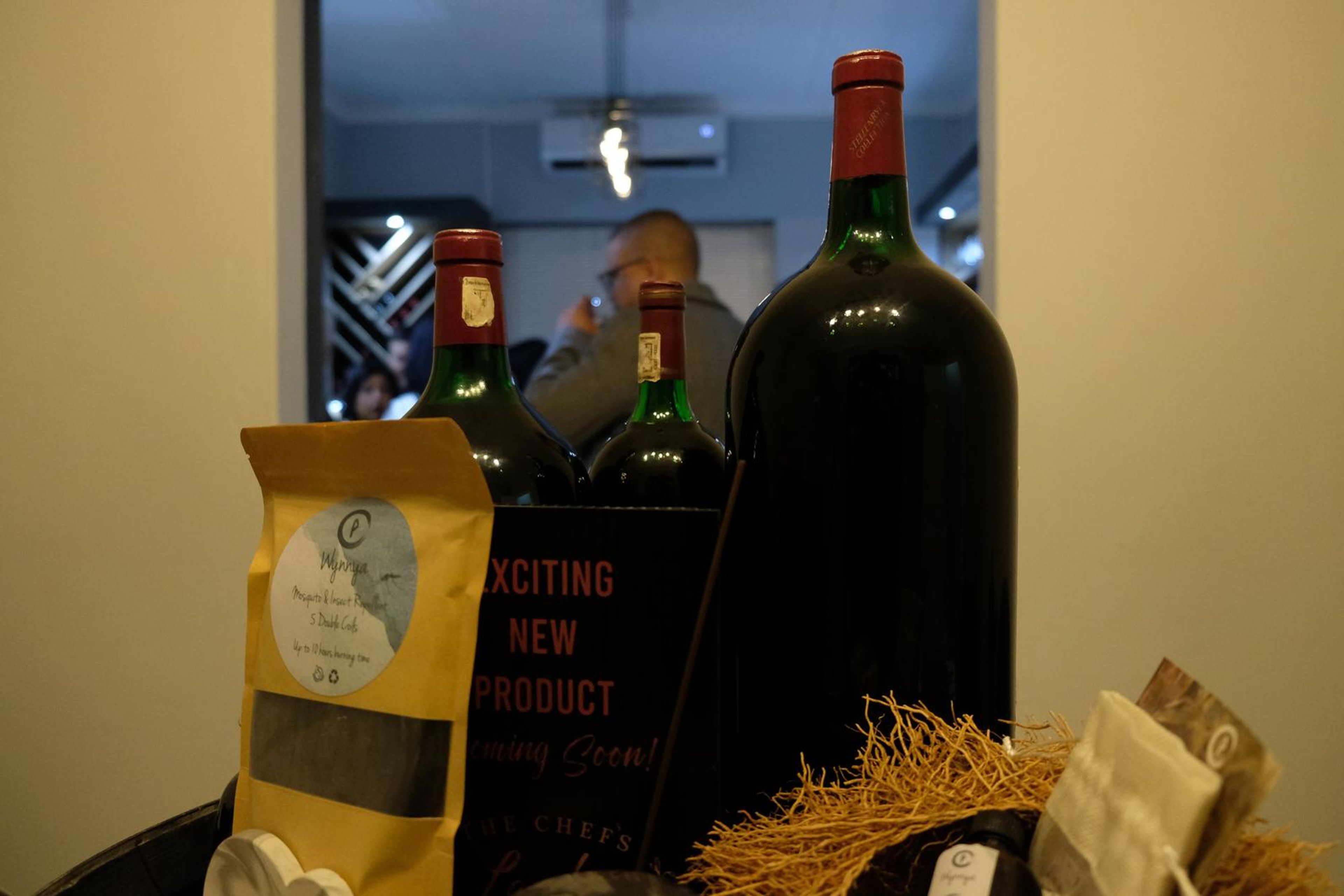 Large wine bottle beside a bag of coffee and an Exciting New Product sign