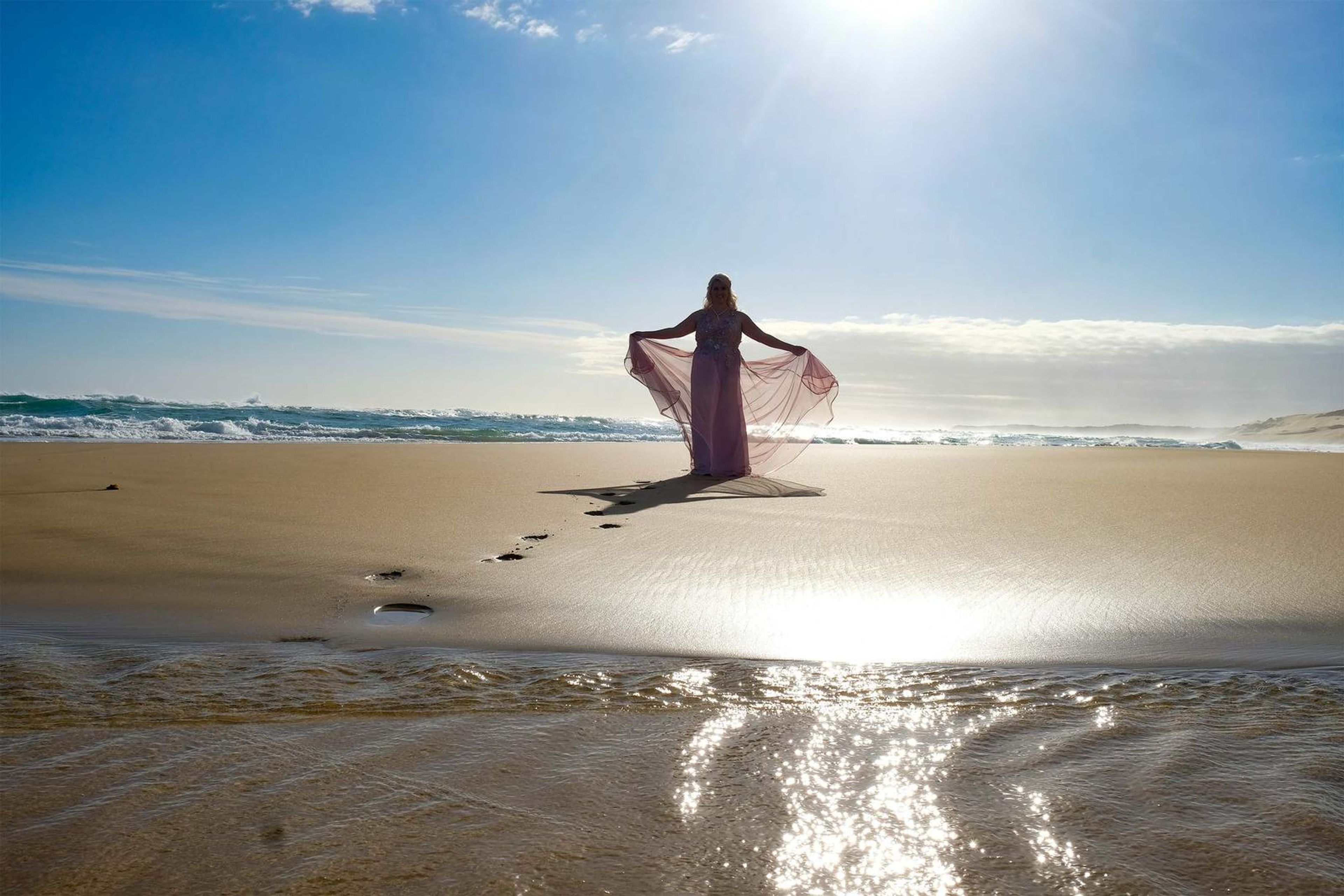 Wide sunlit shoreline with a lone figure and footprints