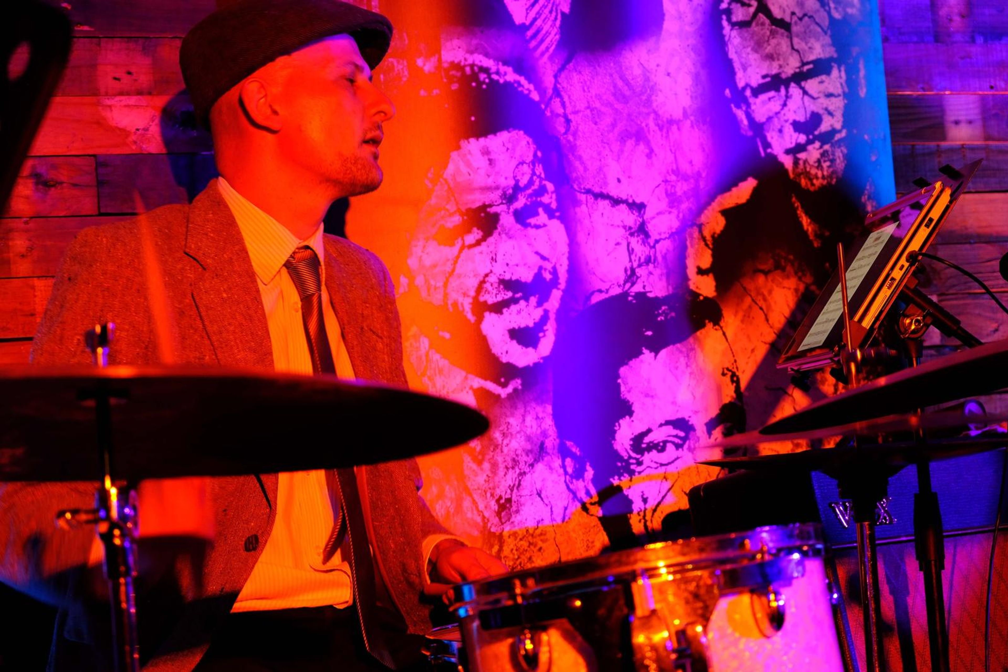 Drummer in a flat cap in front of a colourful mural
