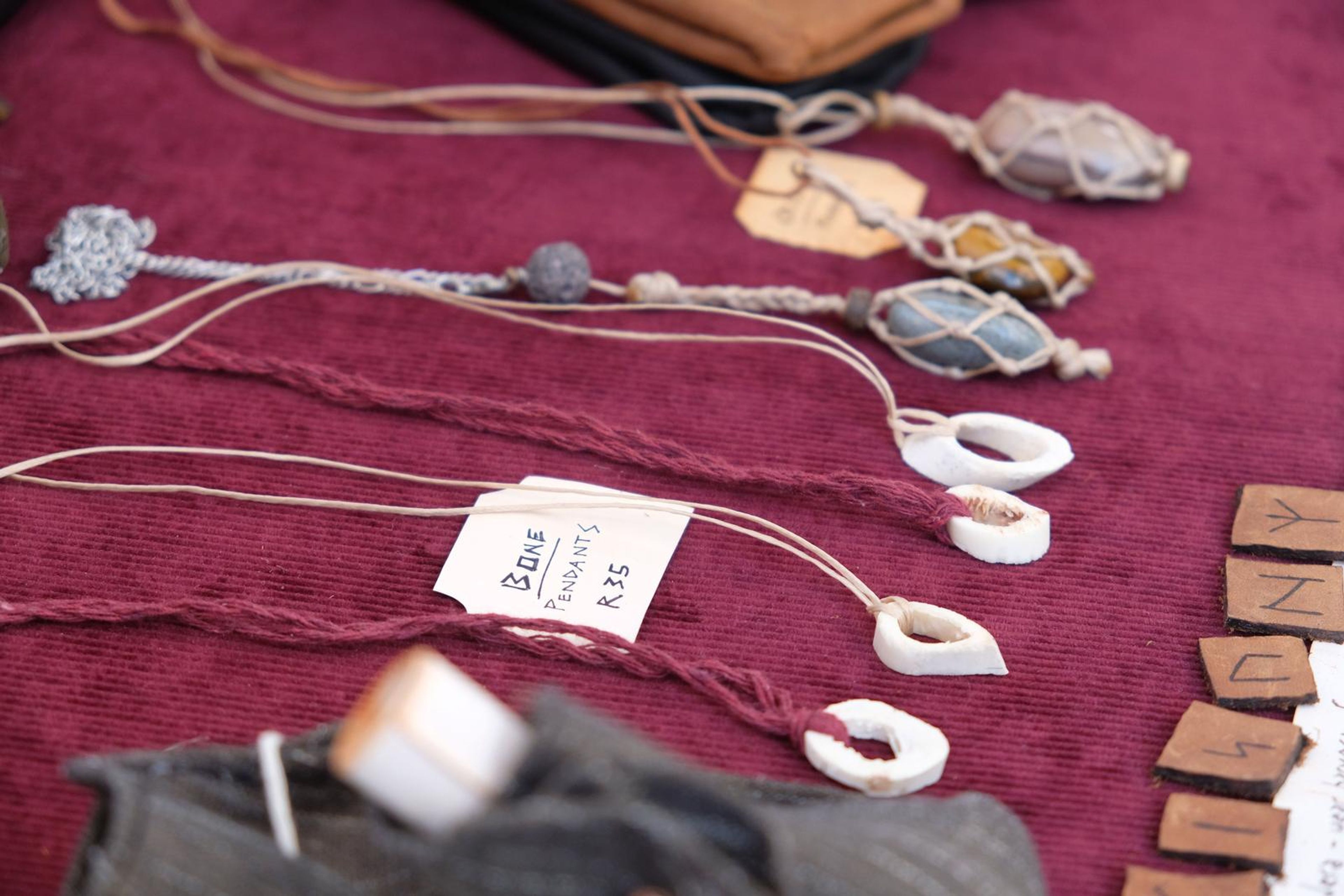 Wire-wrapped crystal and bone pendants with handwritten price tags on maroon cloth