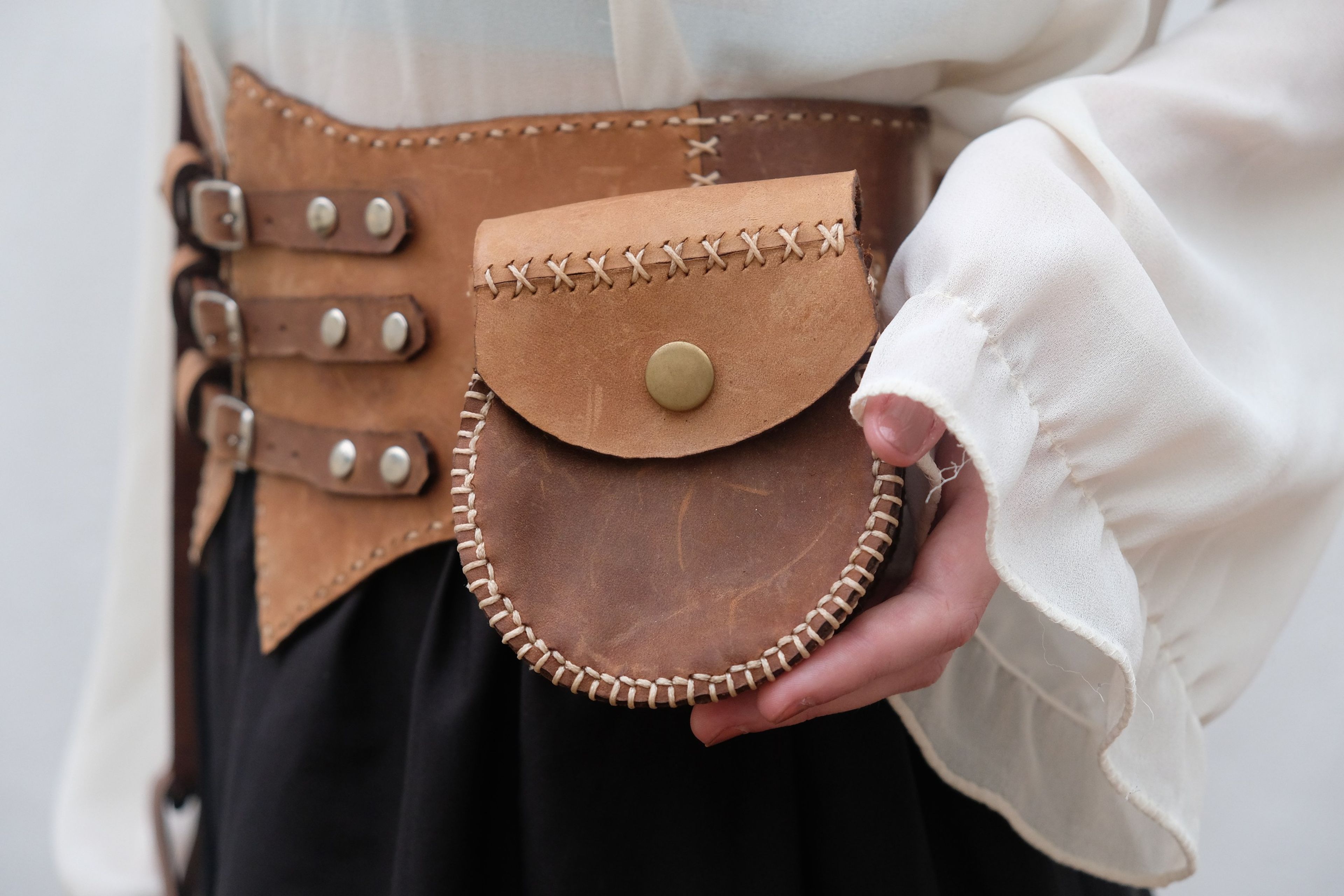 Hand holding the round stitched leather pouch on the corset belt