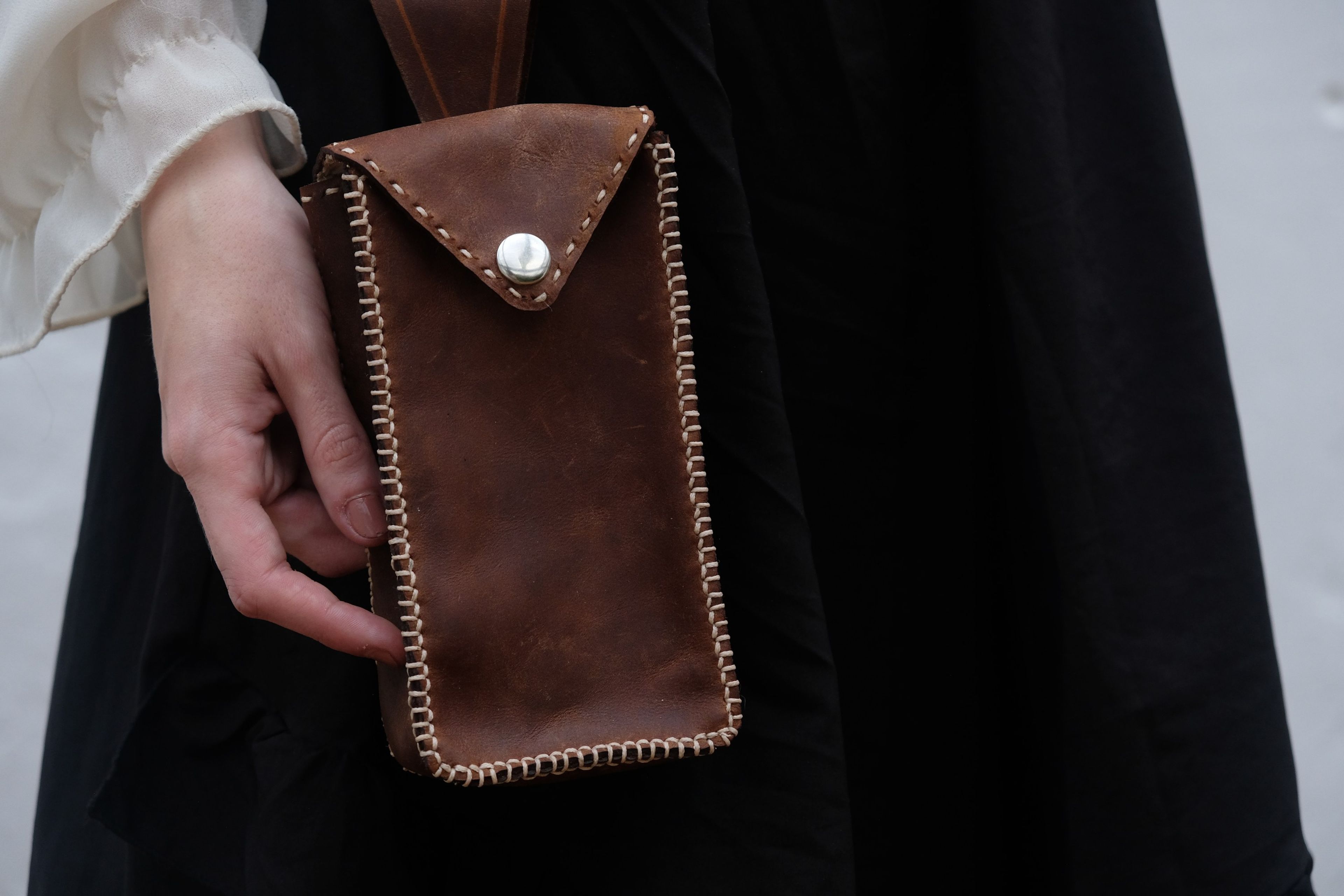 Hand resting on a brown leather phone pouch stitched with cream thread