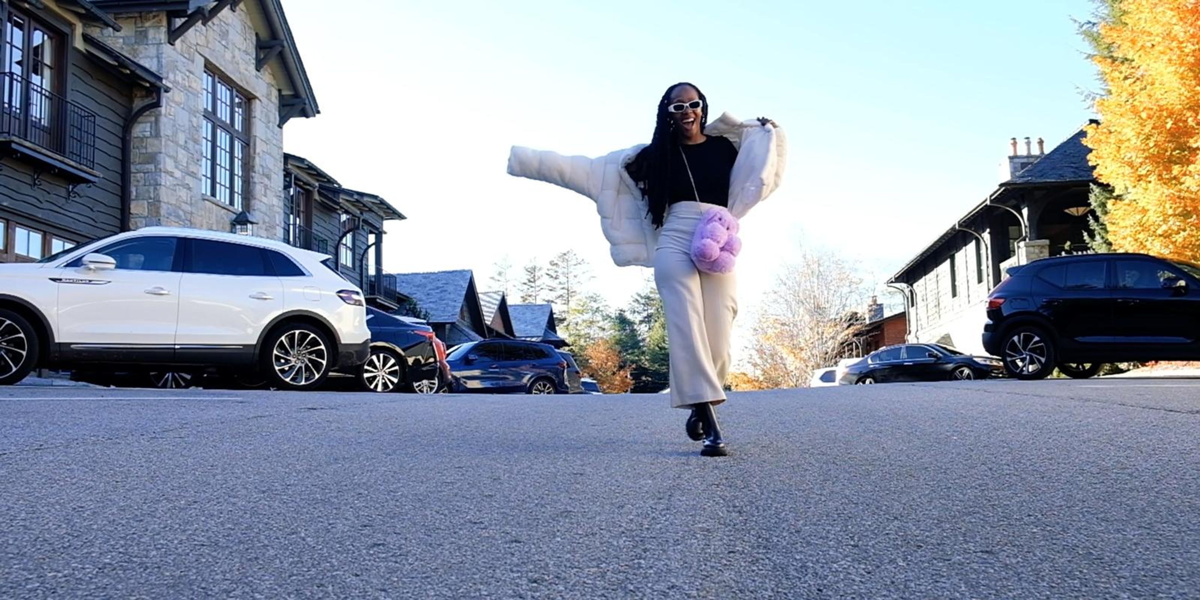 Frame of a woman in a white fur jacket jumping with arms spread on an autumn street