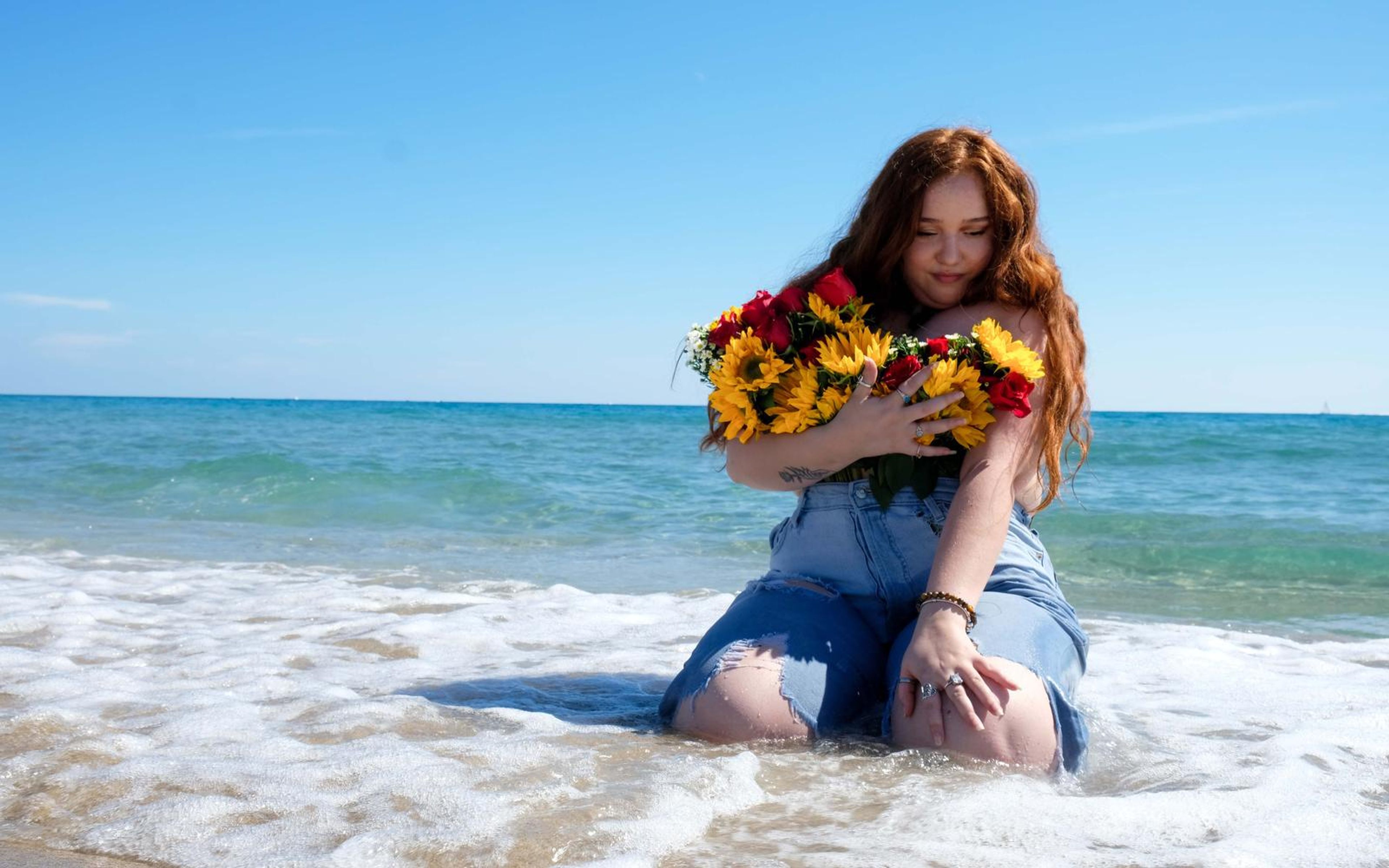 Model sitting in white sea foam with the bouquet held close, one hand resting on her knee