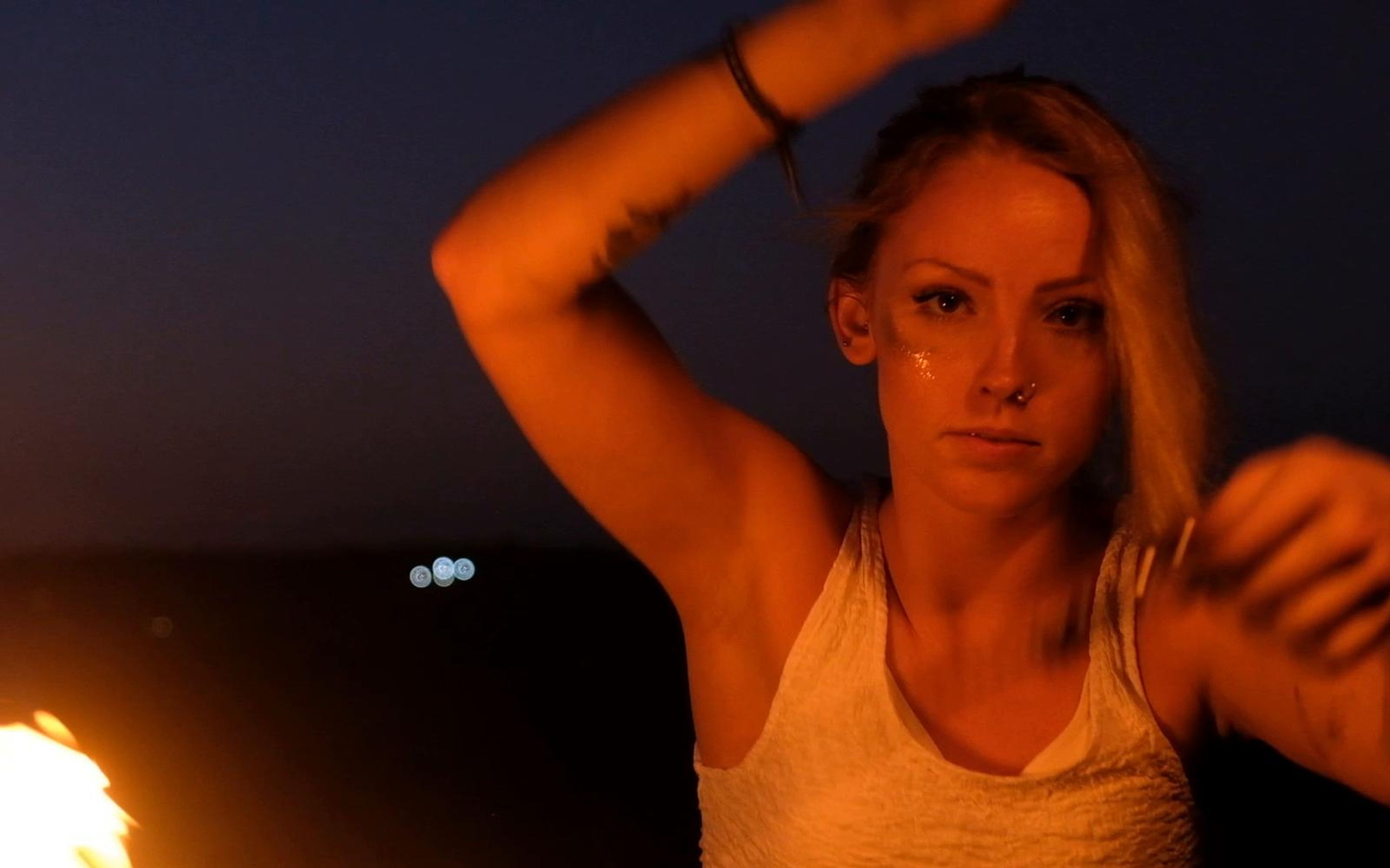 Blonde woman in a white top with her arm raised to her head, looking into the lens