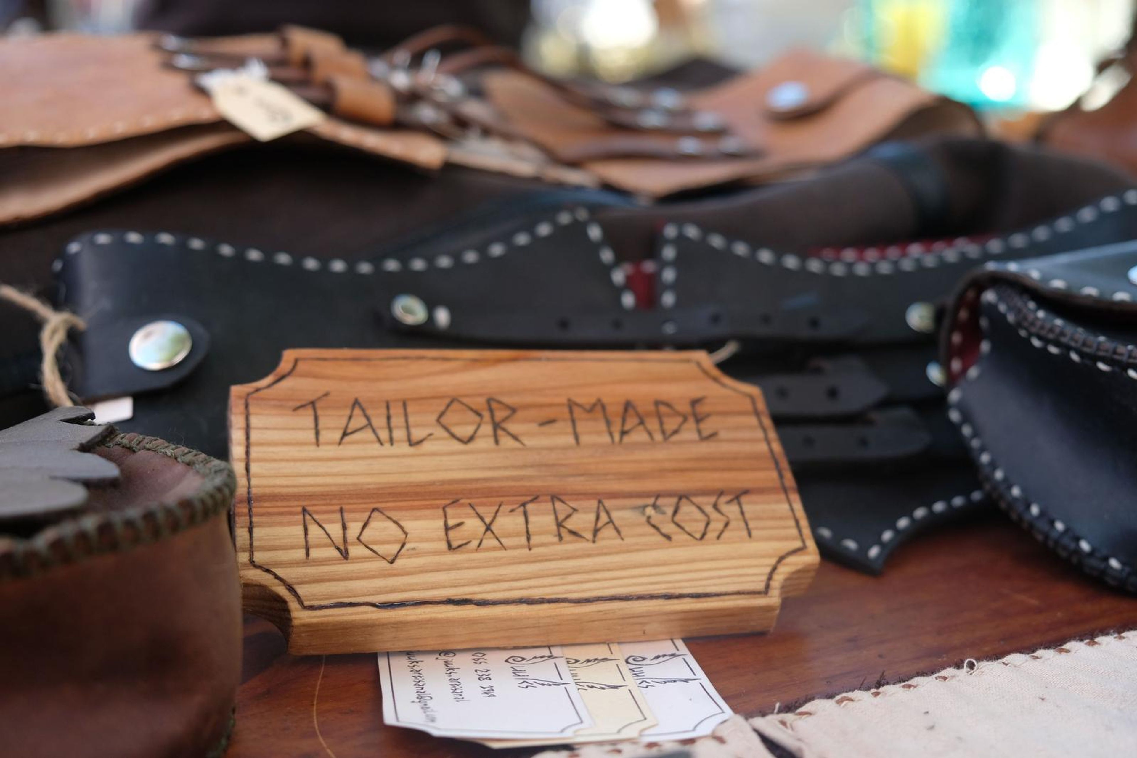 Black leather pouch and corset belts beside a Tailor-Made No Extra Cost sign
