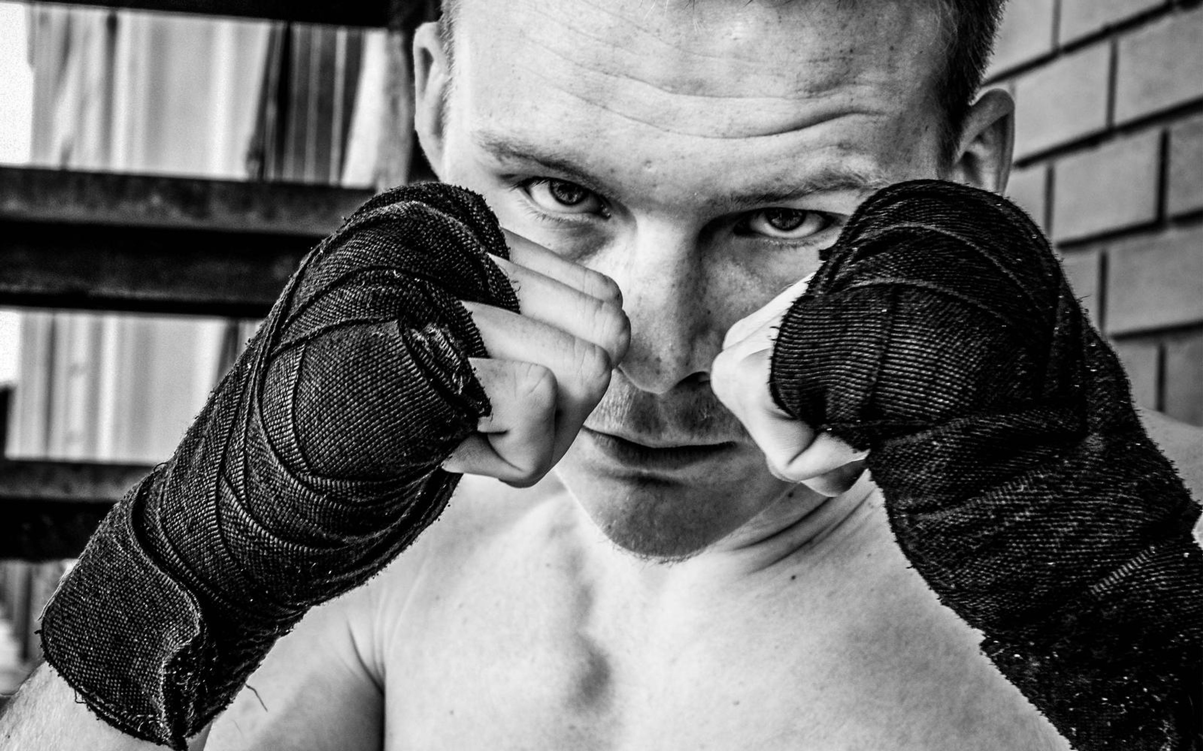 Black and white close-up of a man peering over two wrapped fists, intense eyes