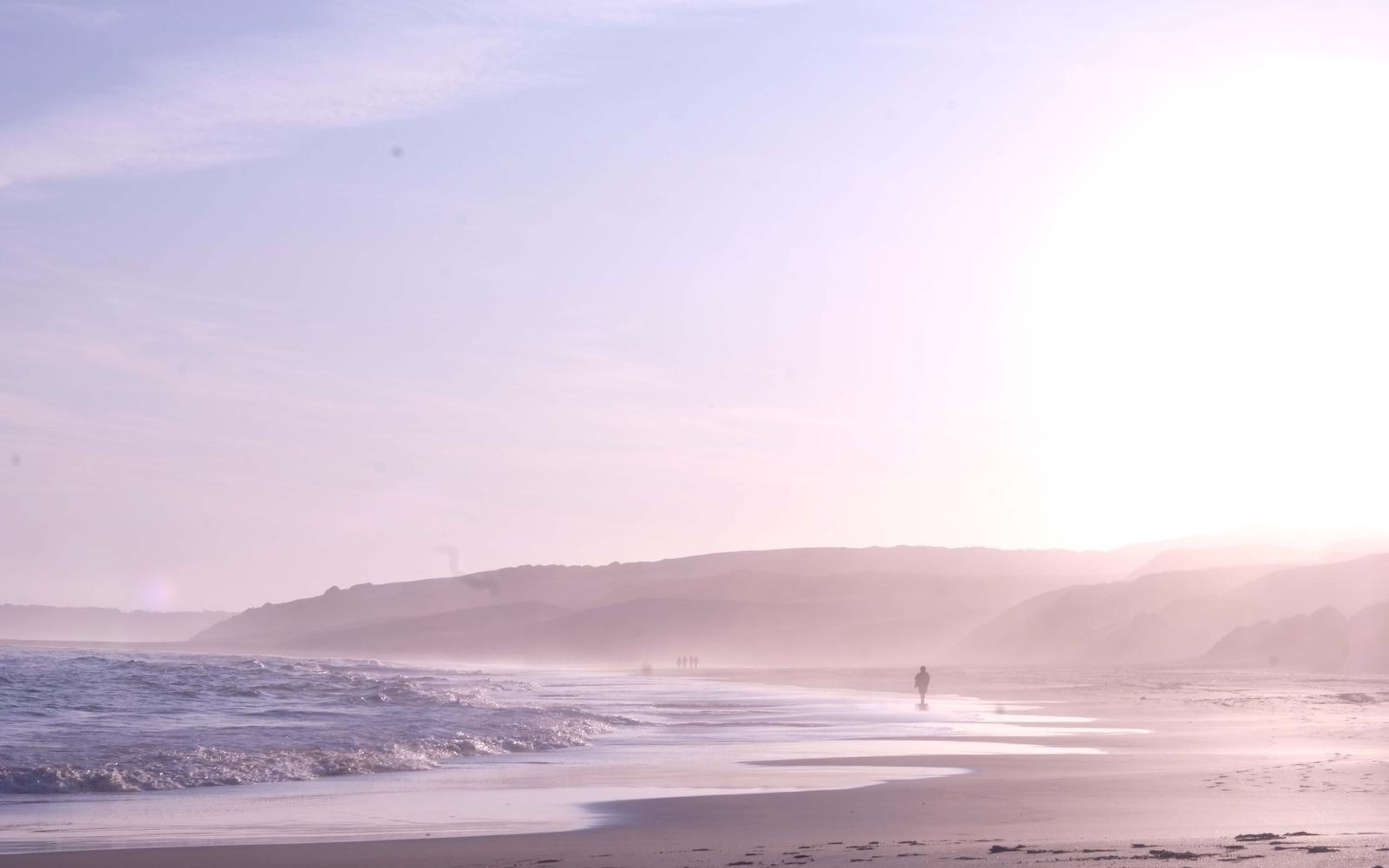 Pink and lilac haze over a long beach with a lone figure far along the waterline