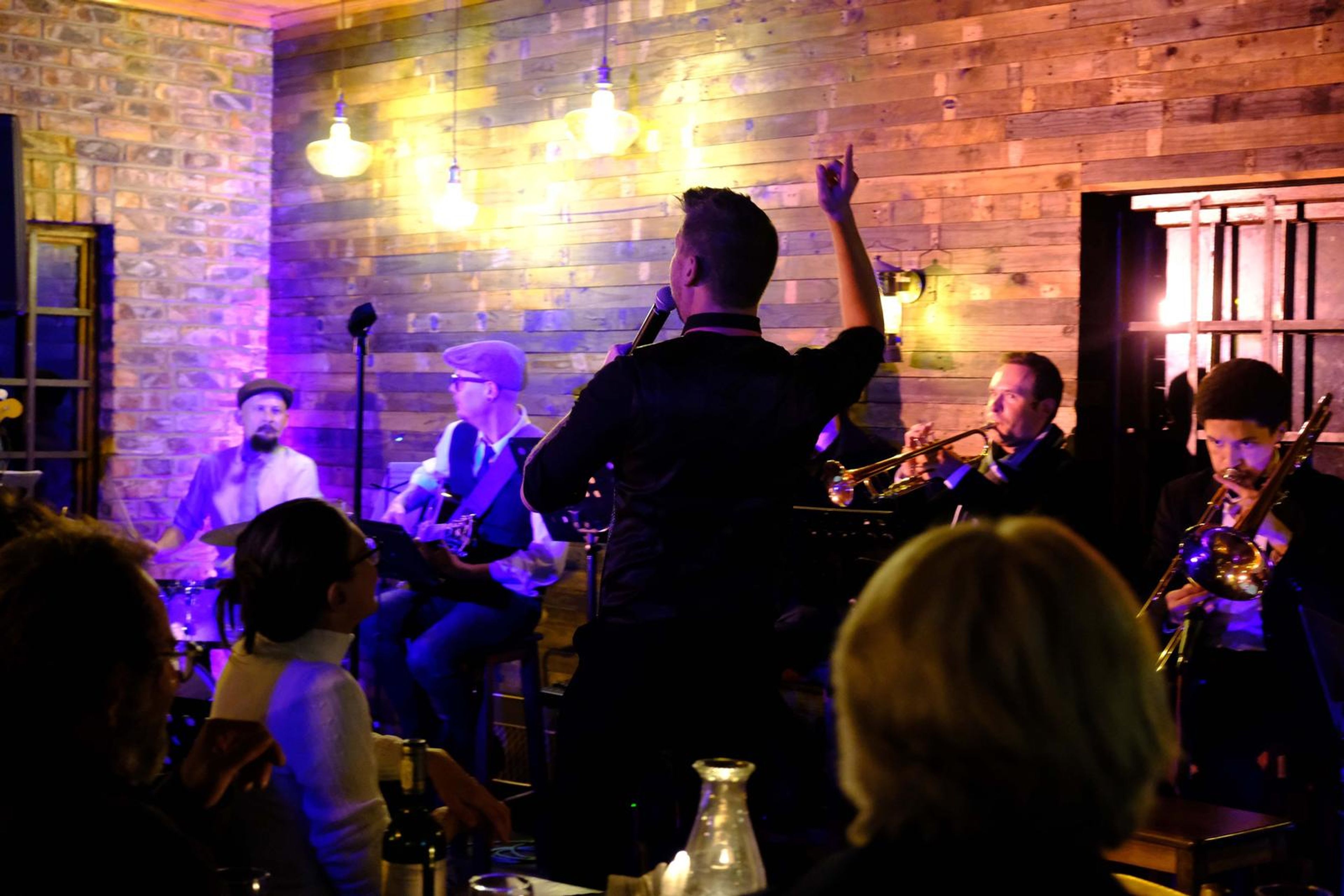 Lead singer pointing up as the band plays in a purple-lit room