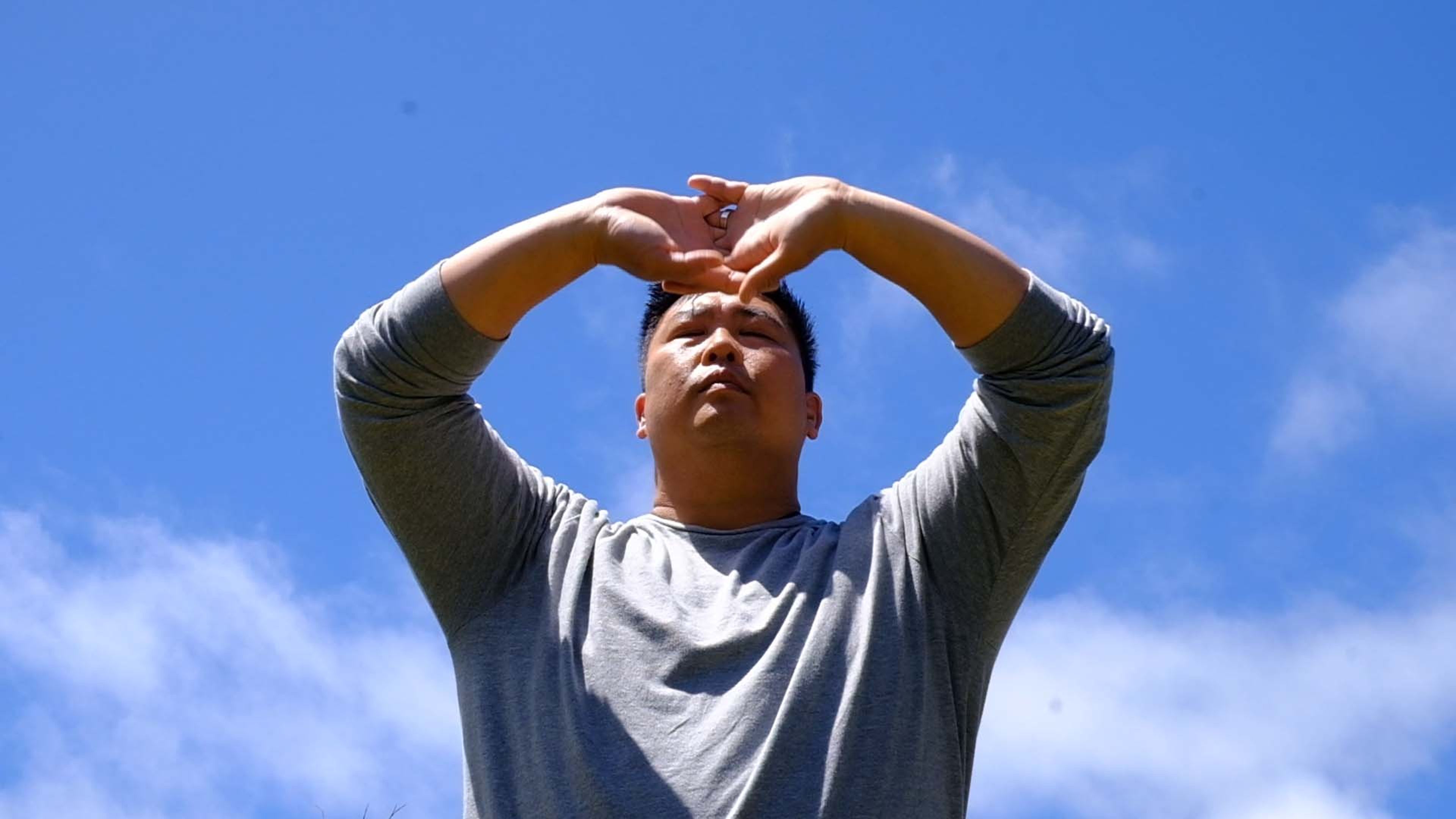 Man with his hands overhead against a blue sky during an outdoor movement session