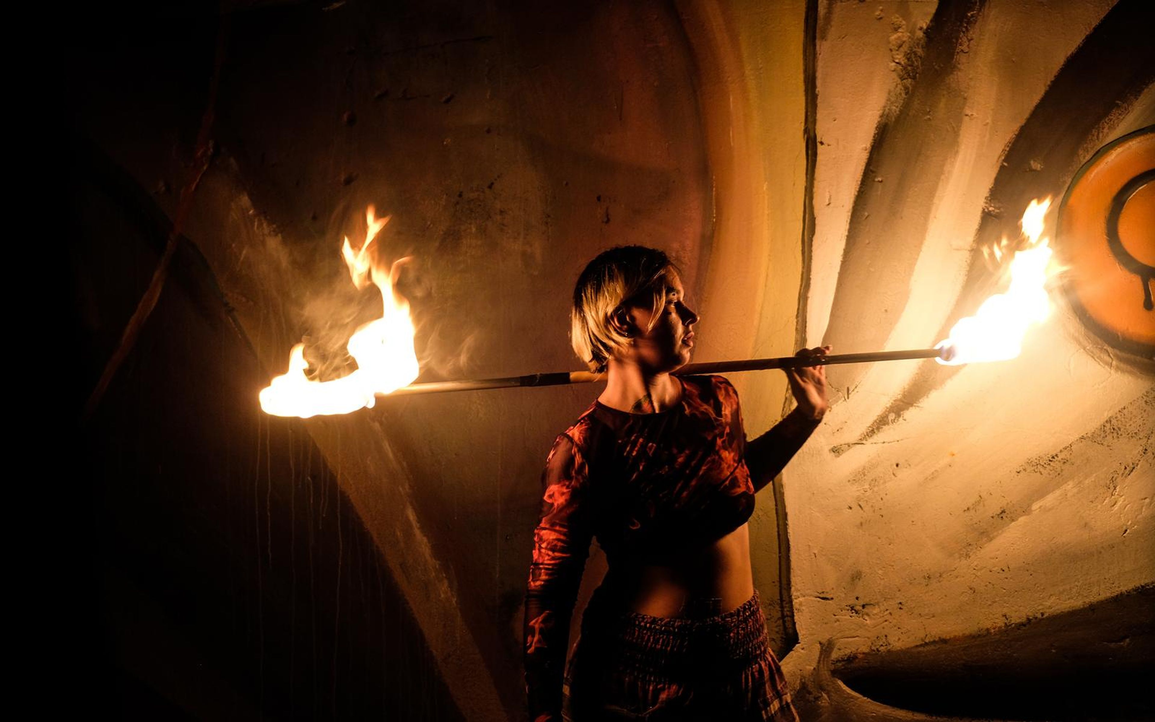 Performer in profile with a burning staff across the shoulders and a round emblem at the right