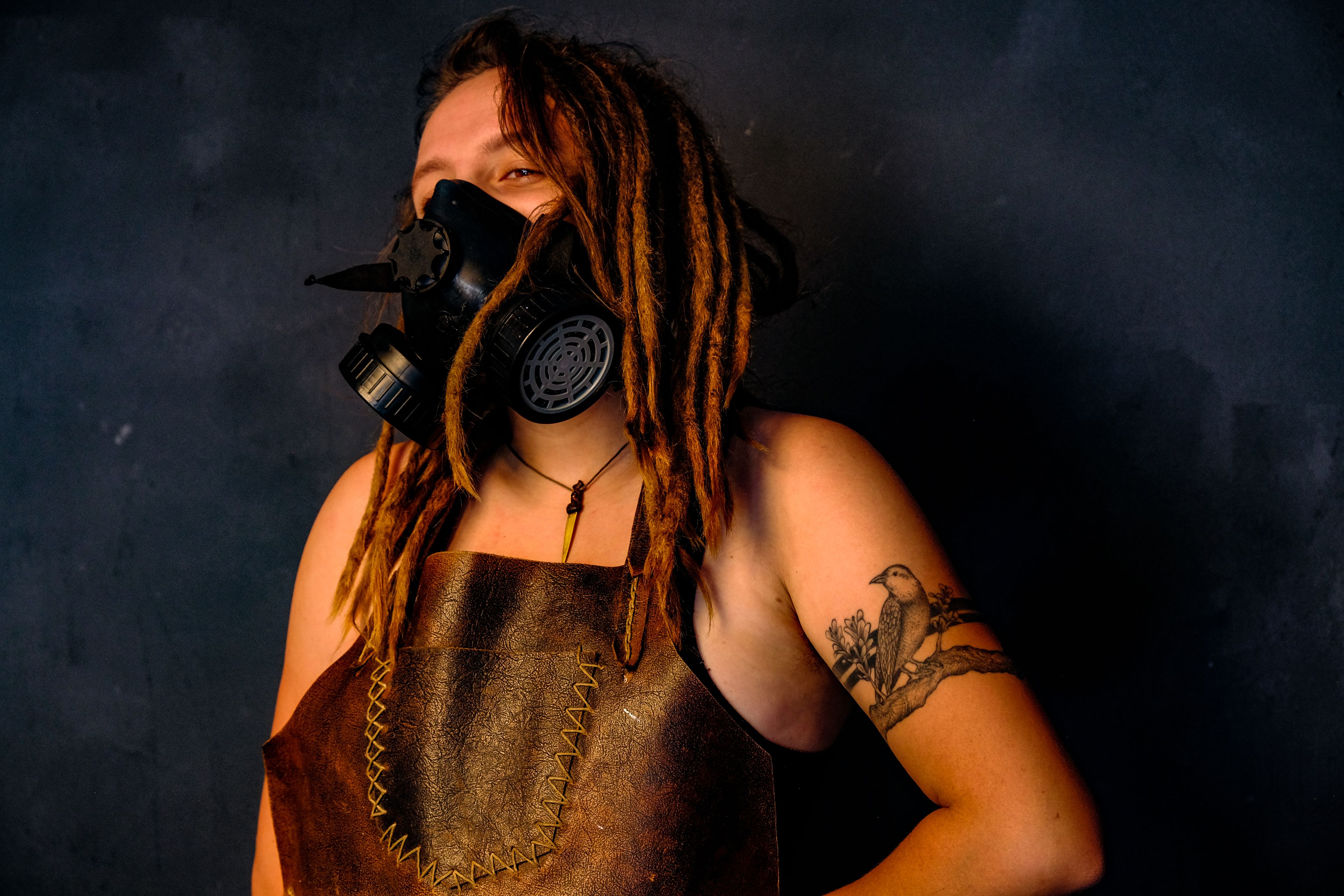 Warm-toned portrait, gas mask lowered, subject smiling, wearing a leather apron