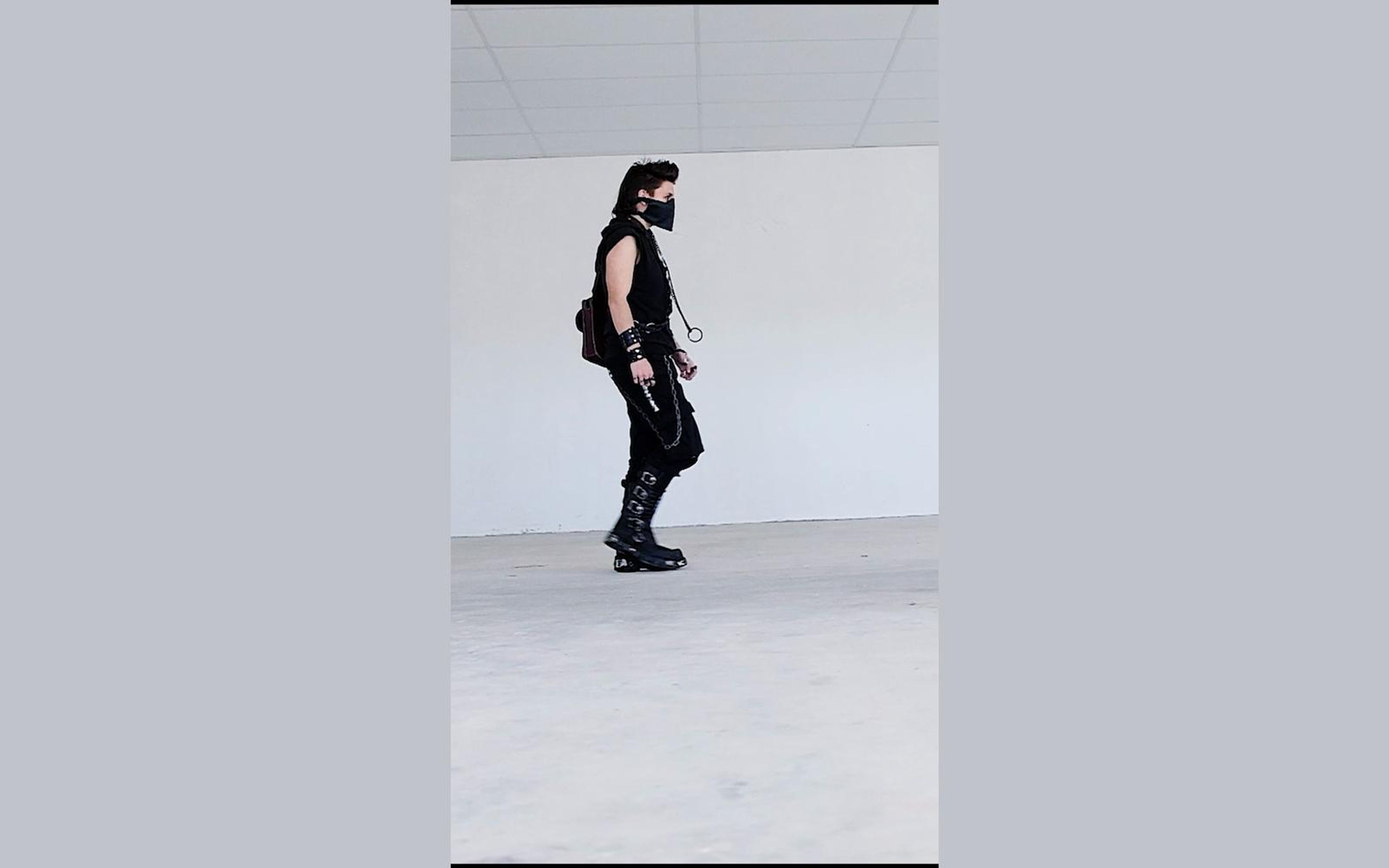 Masked figure paused between steps in side view with a small satchel on the back