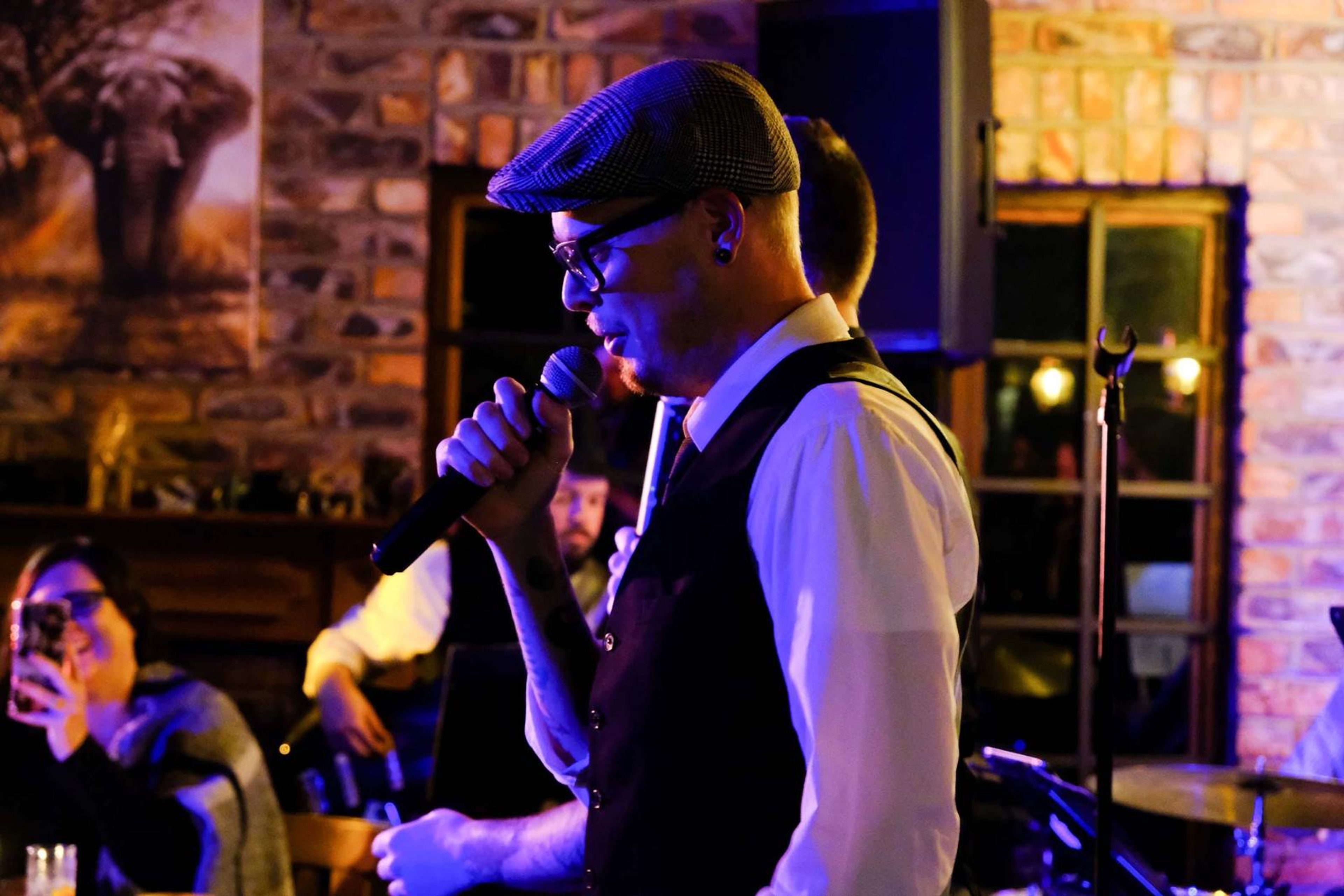 Singer in a flat cap and waistcoat singing into the microphone