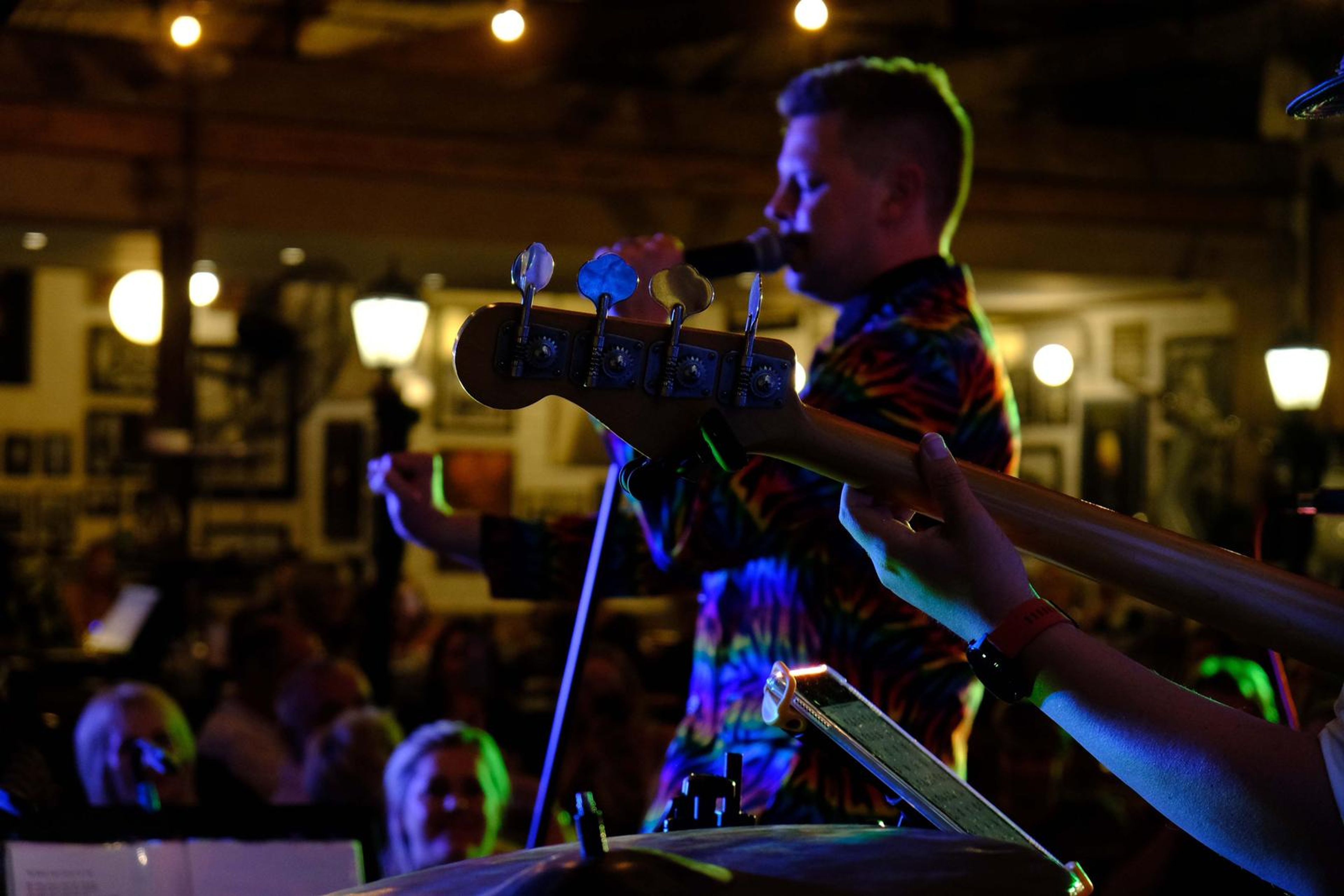 Bassist in a rainbow jacket playing as guests film him