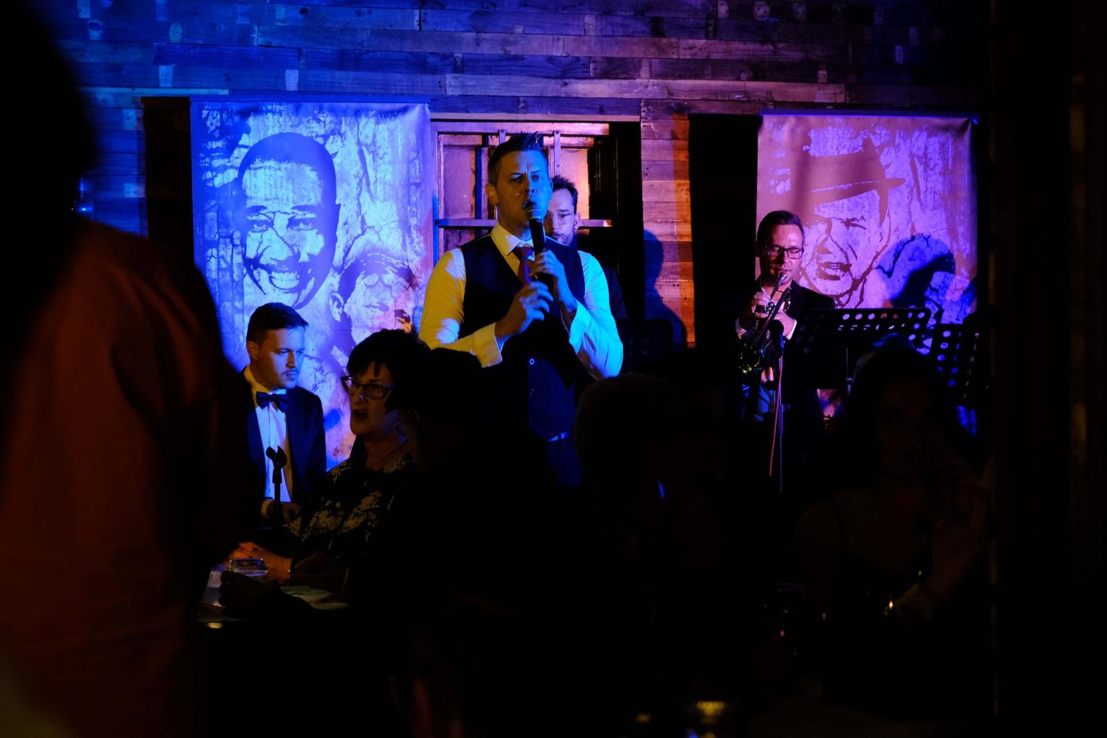 Singer in a yellow waistcoat with horn players beneath the murals