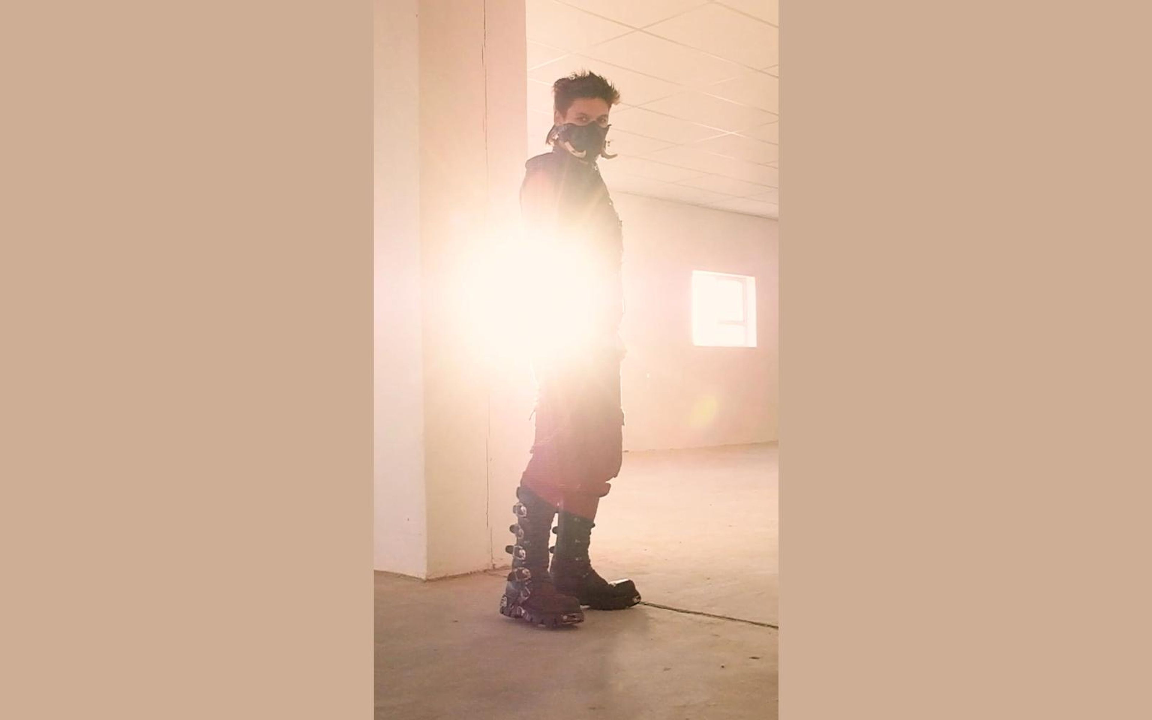 Masked figure in side view fading into sunlit haze with spiked New Rock boots on the concrete floor