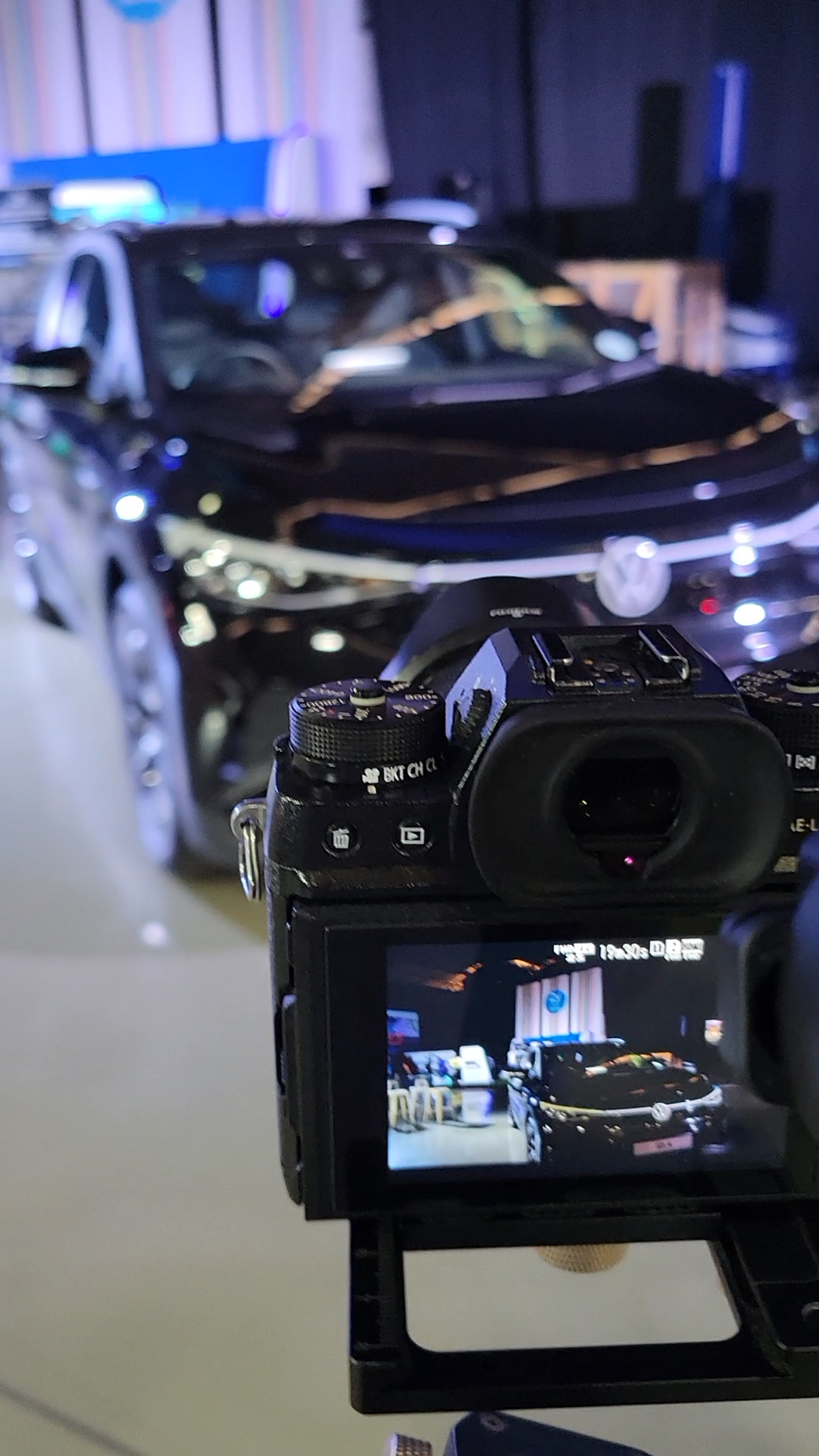 Behind the scenes at the expo, a camera in front of a black Volkswagen on display