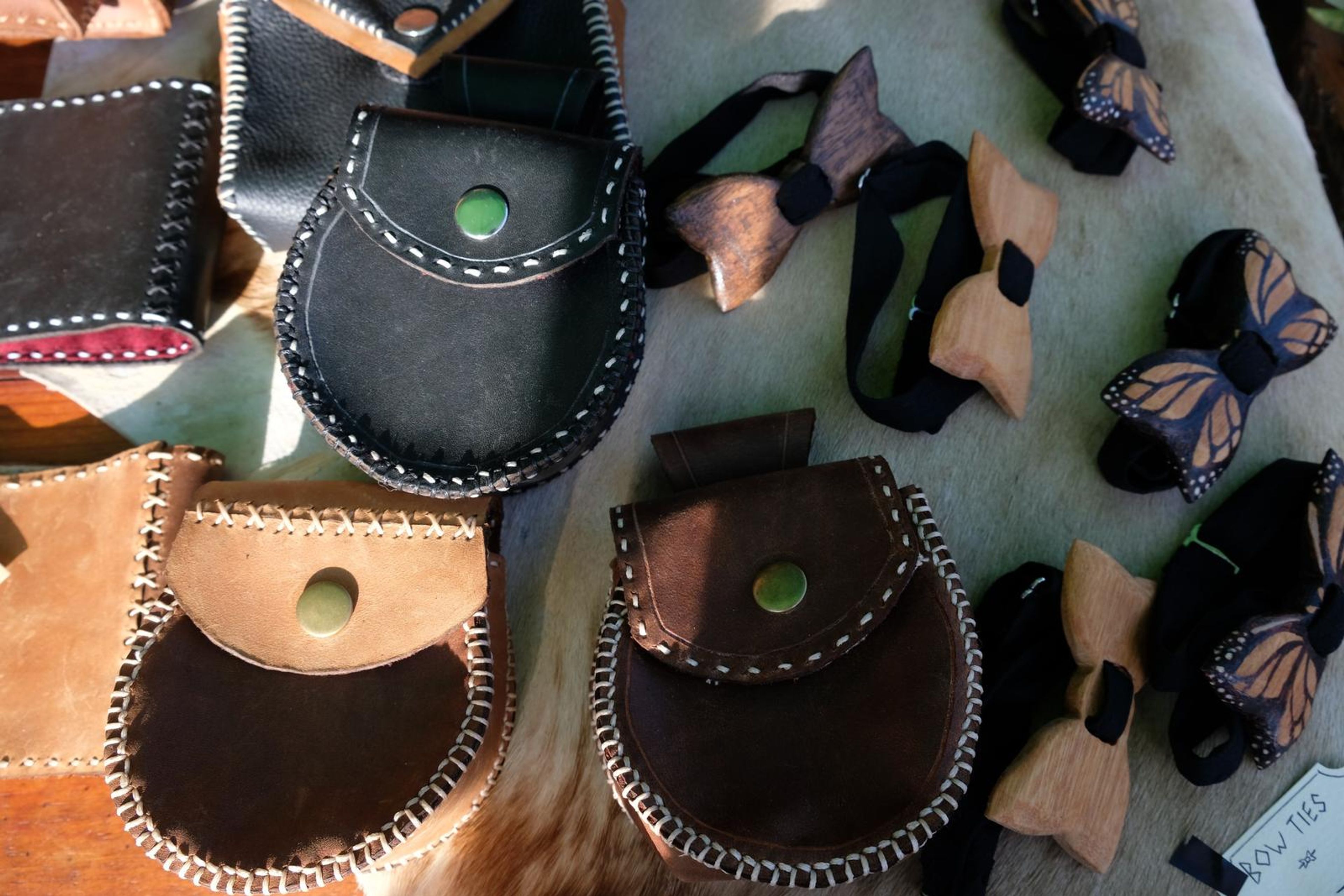 Leather pouches and carved wooden bow ties on a hide from above