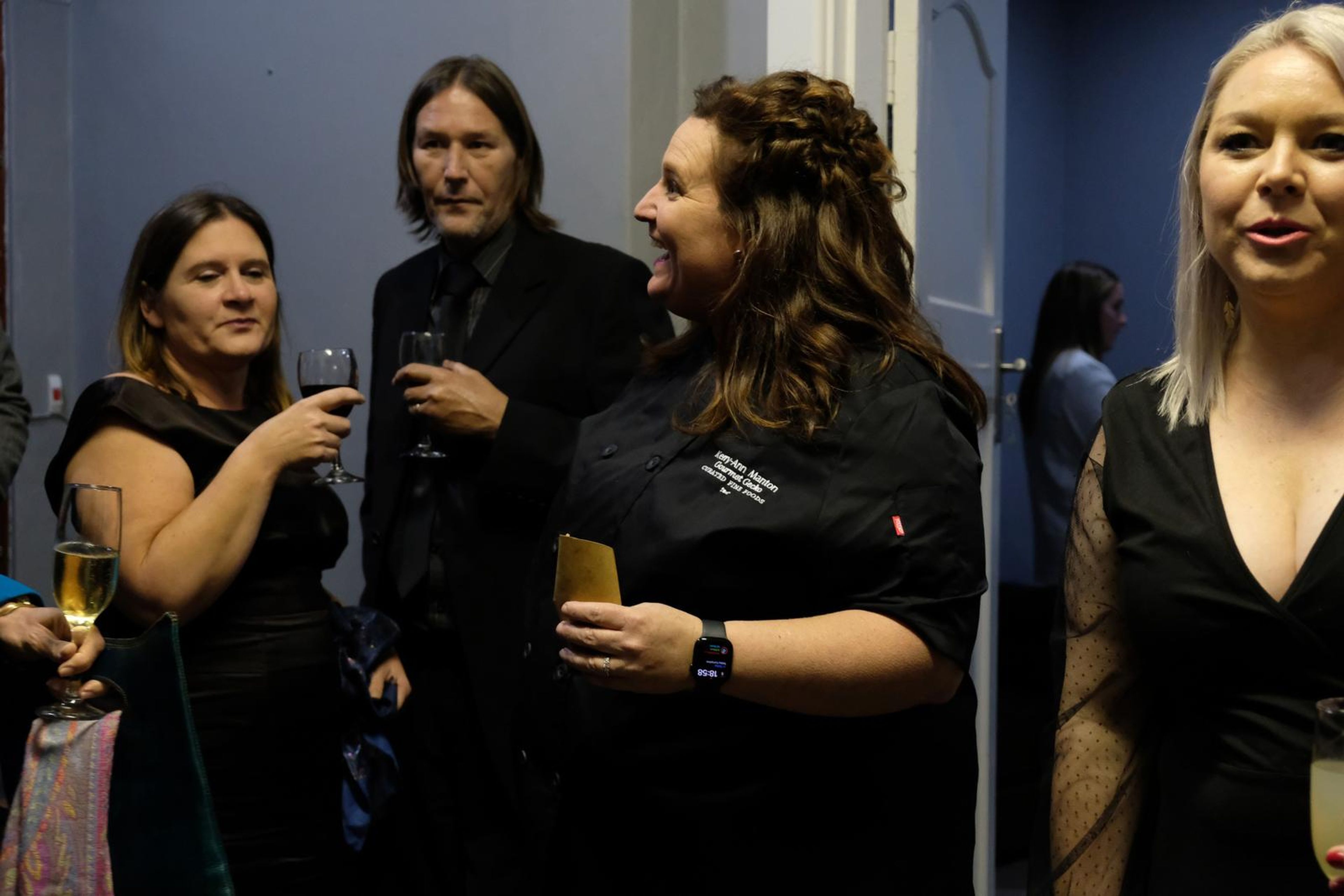Chef in a black Chef's Larder jacket laughing with guests holding champagne