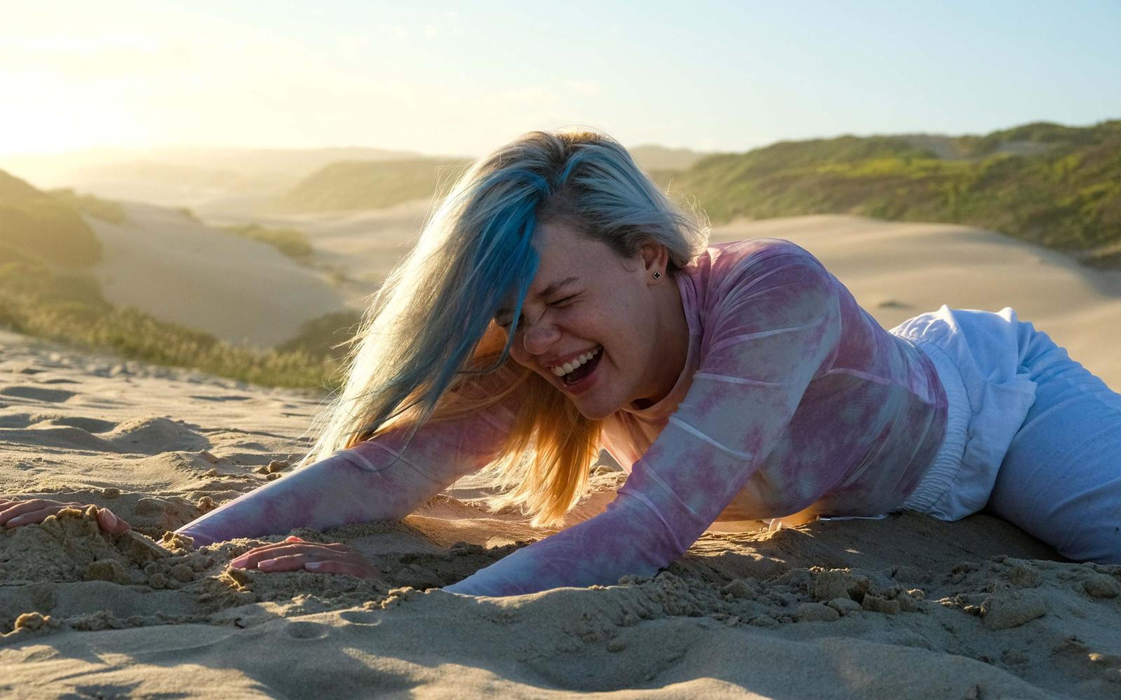 Woman laughing hard while leaning on the sand with hair blowing across her face