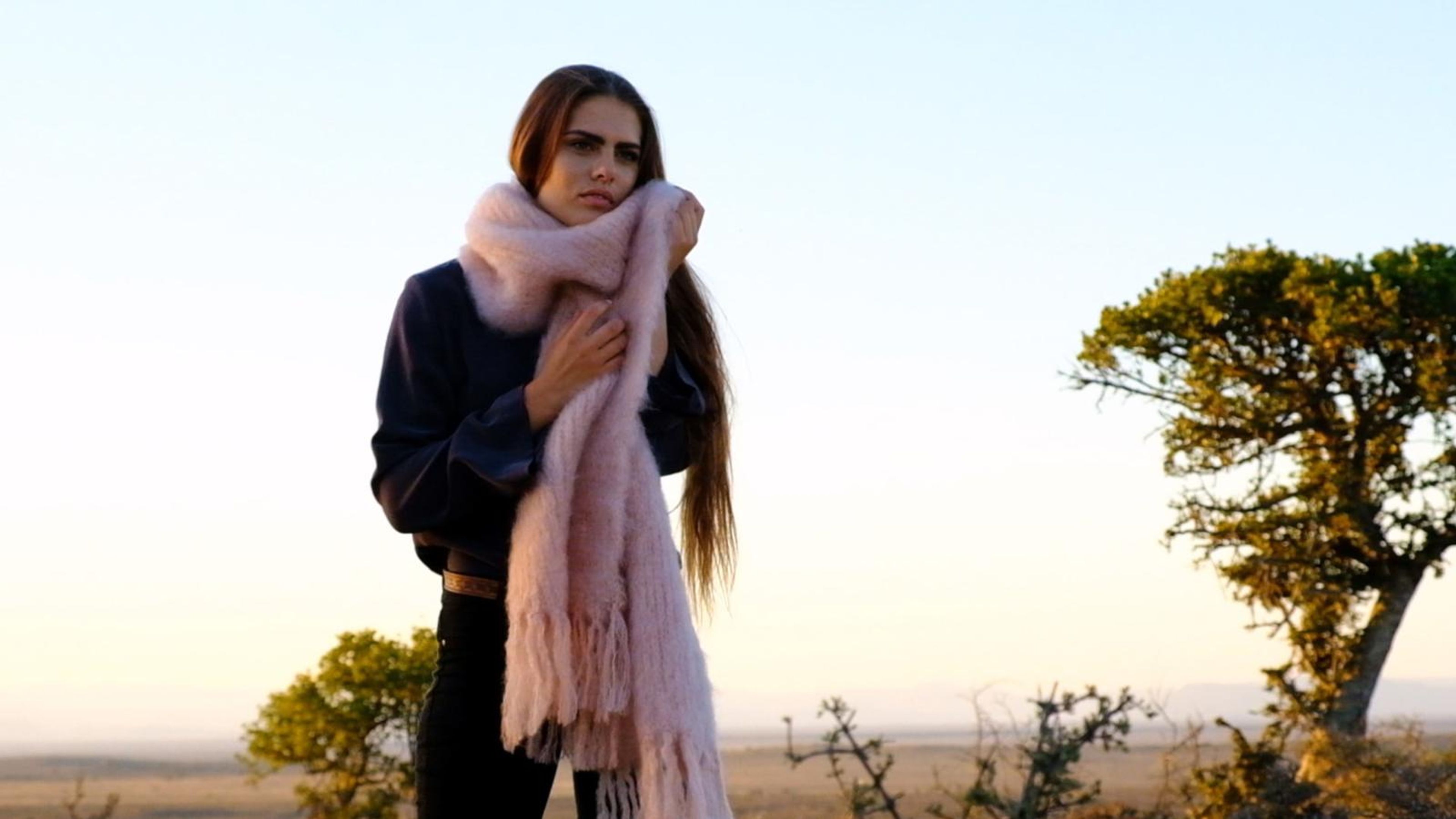 Model holding a long pink mohair scarf against a quiver tree