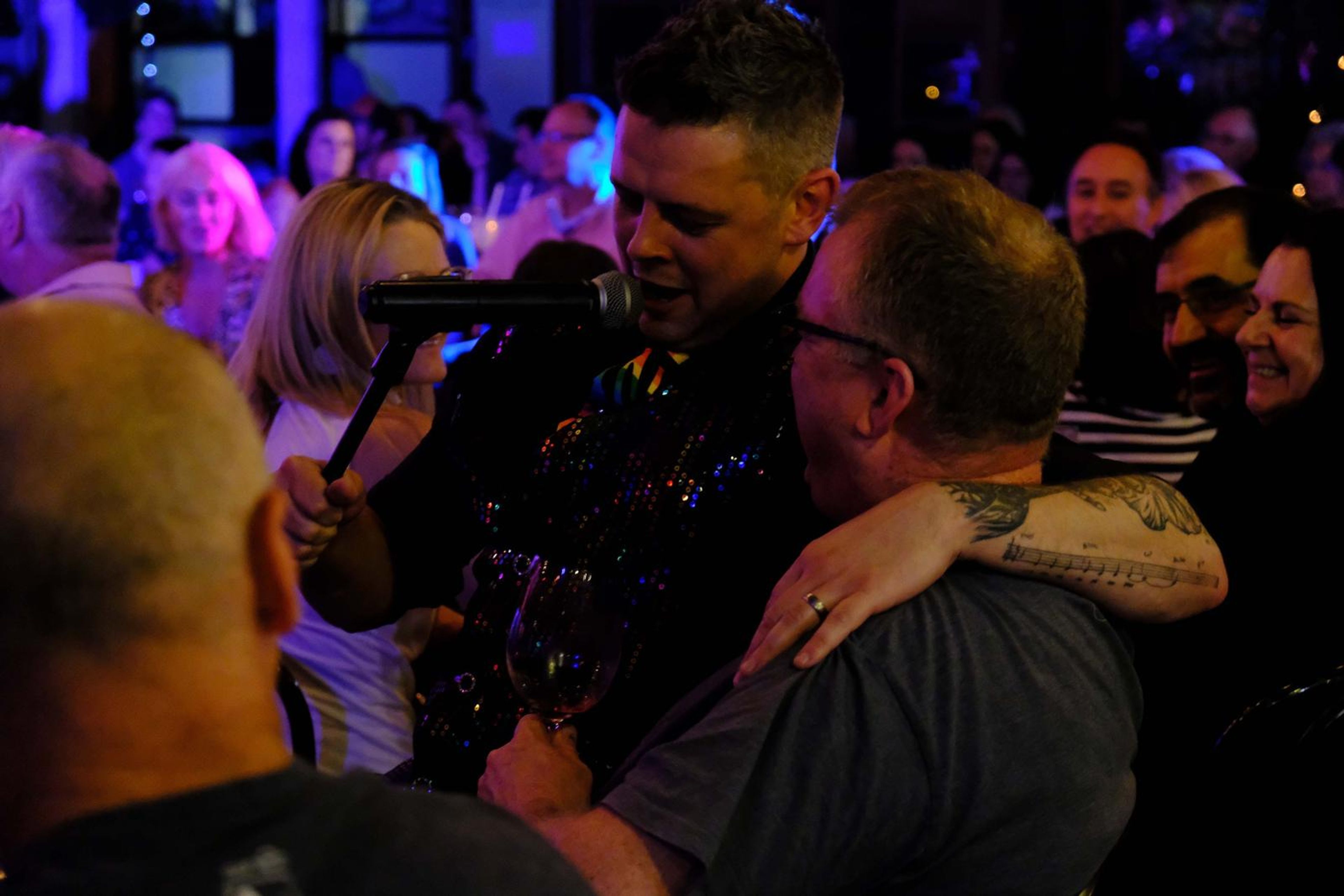 Singer leaning on a guest's shoulder as the table laughs
