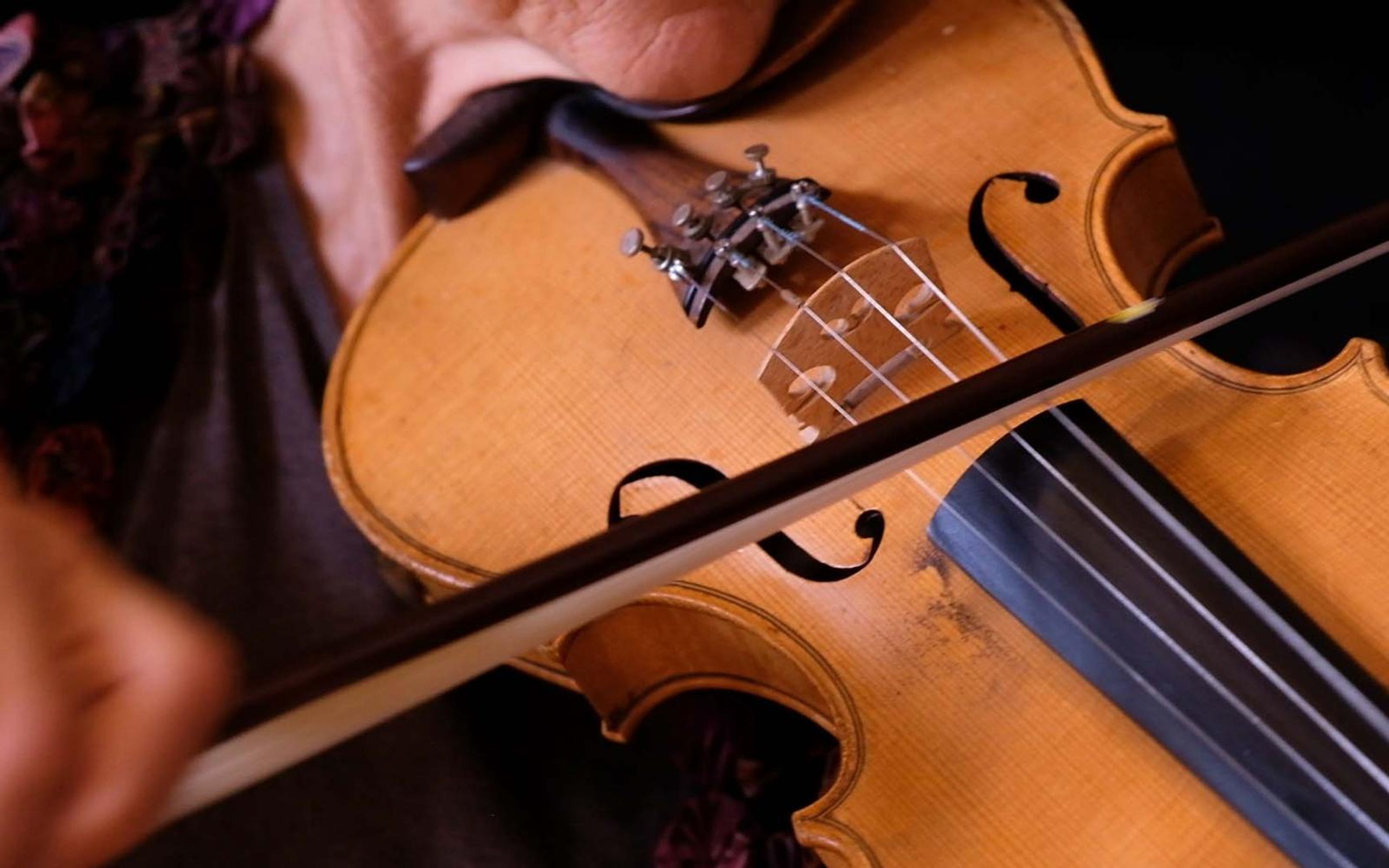 Close view of hands bowing a violin, warm wood against dark clothing