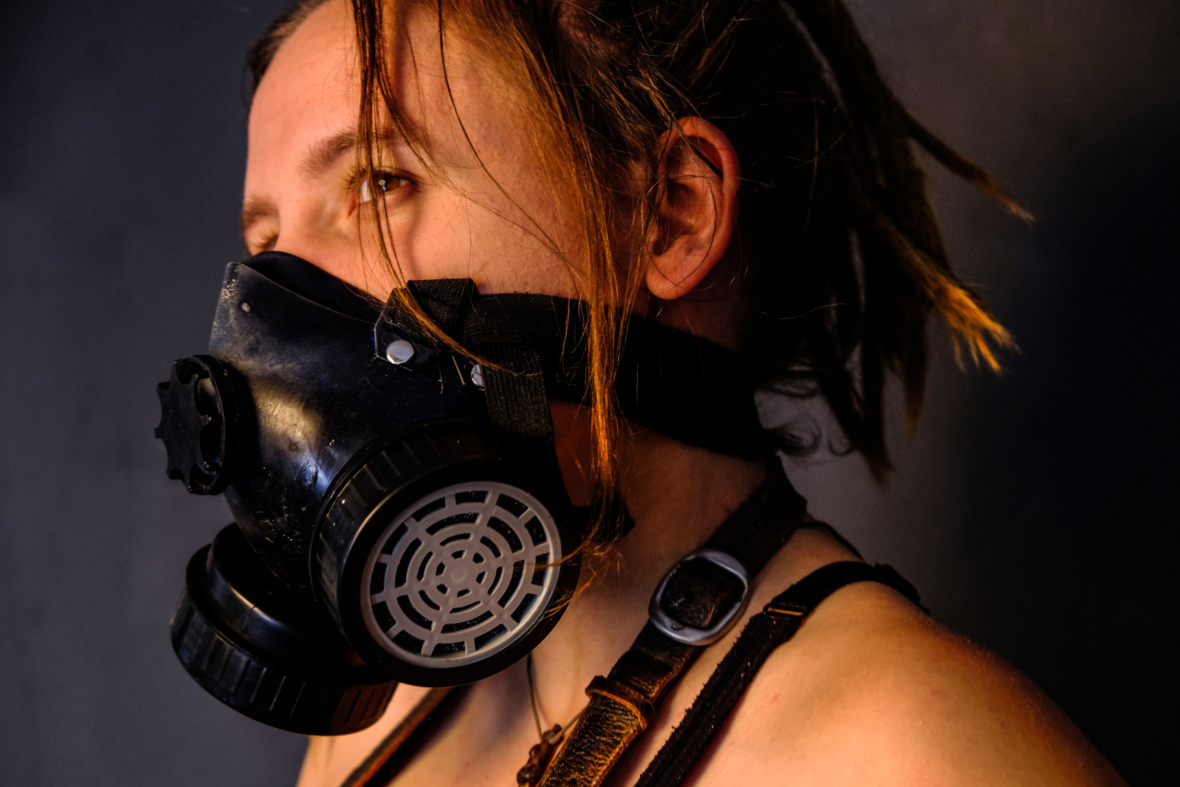 Warm-toned side profile portrait, subject wearing a gas mask and leather harness strap