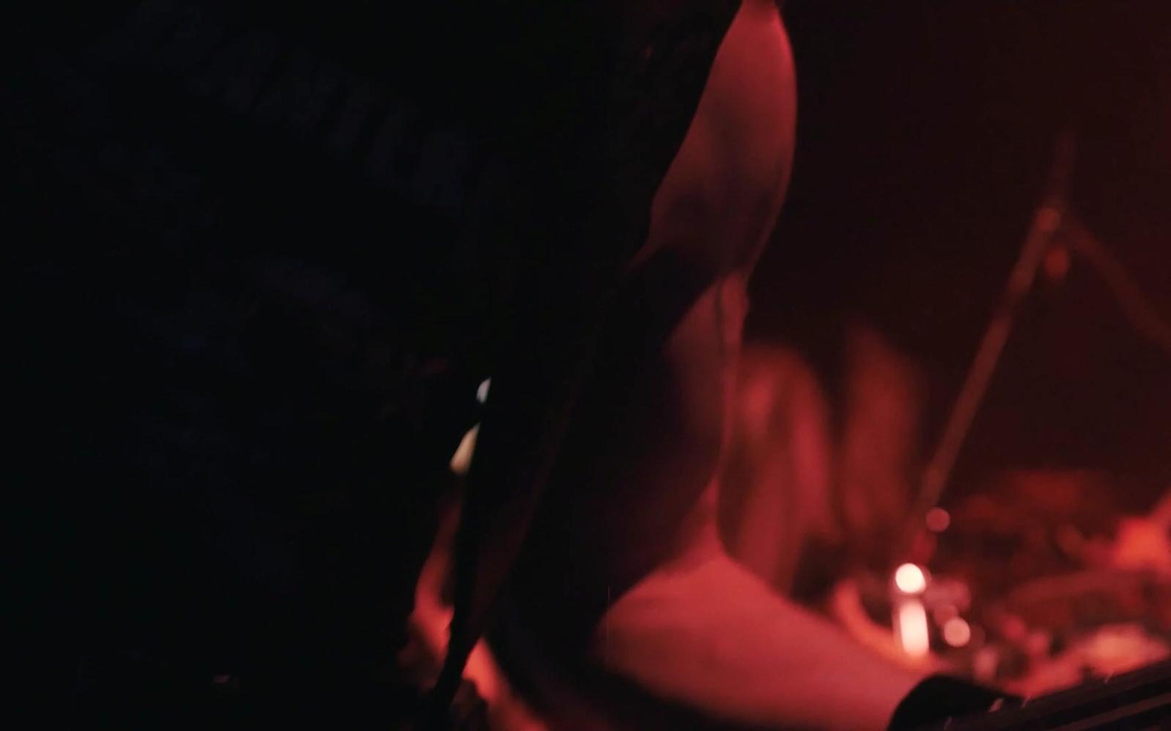 Dark stage silhouette lit red with a musician and drum kit blurred behind