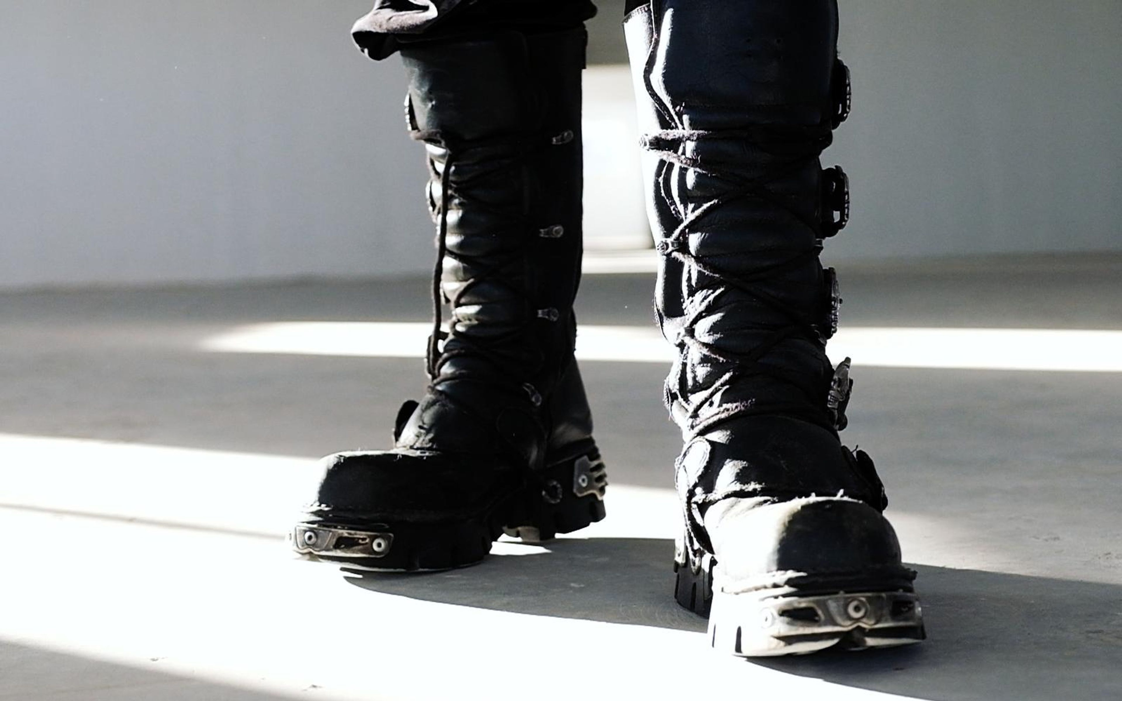 Two black buckled boots stepping forward through bright window light on a pale floor, low angle
