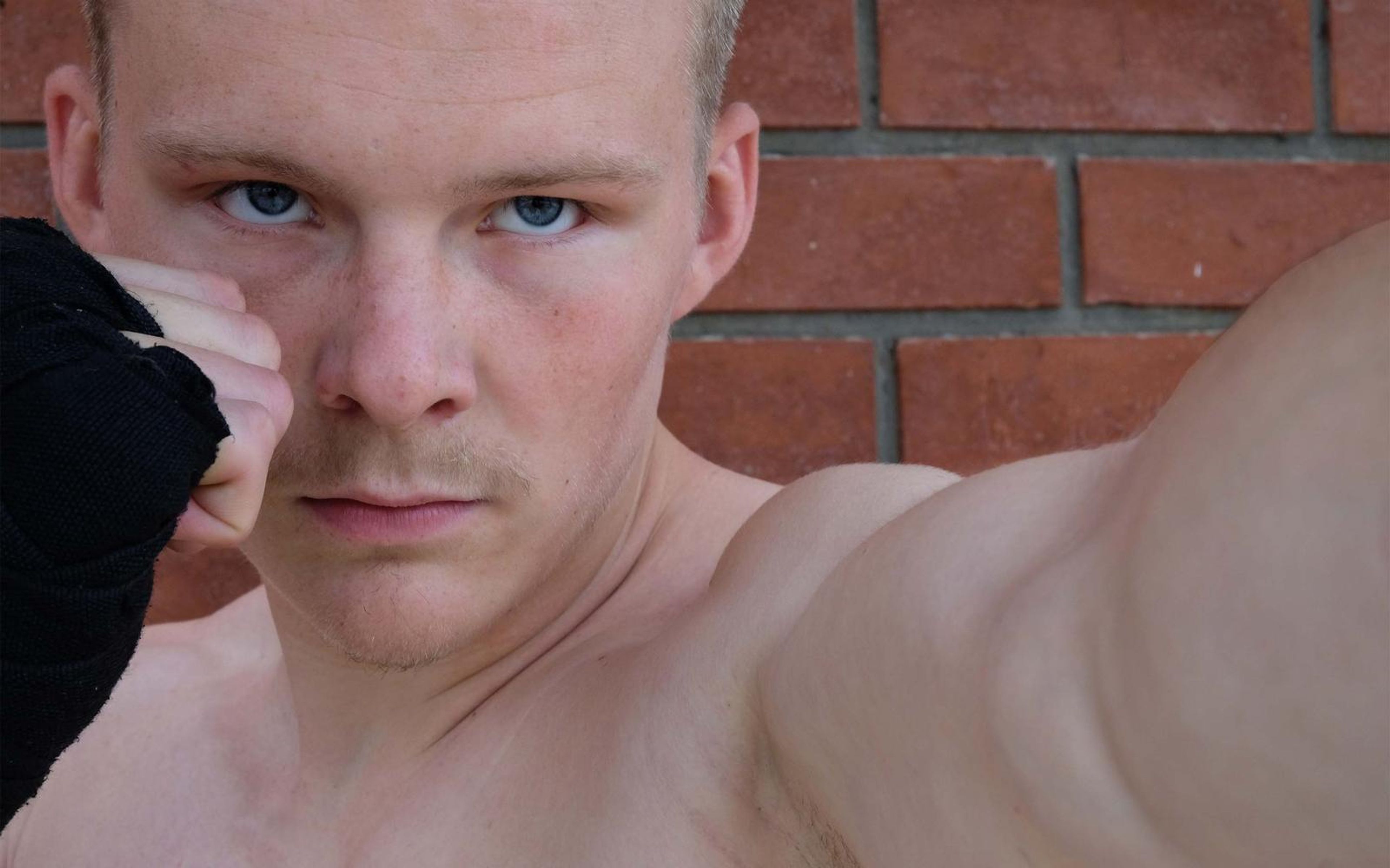 Extreme close-up of the fighter's stare over a raised wrapped fist against red brick