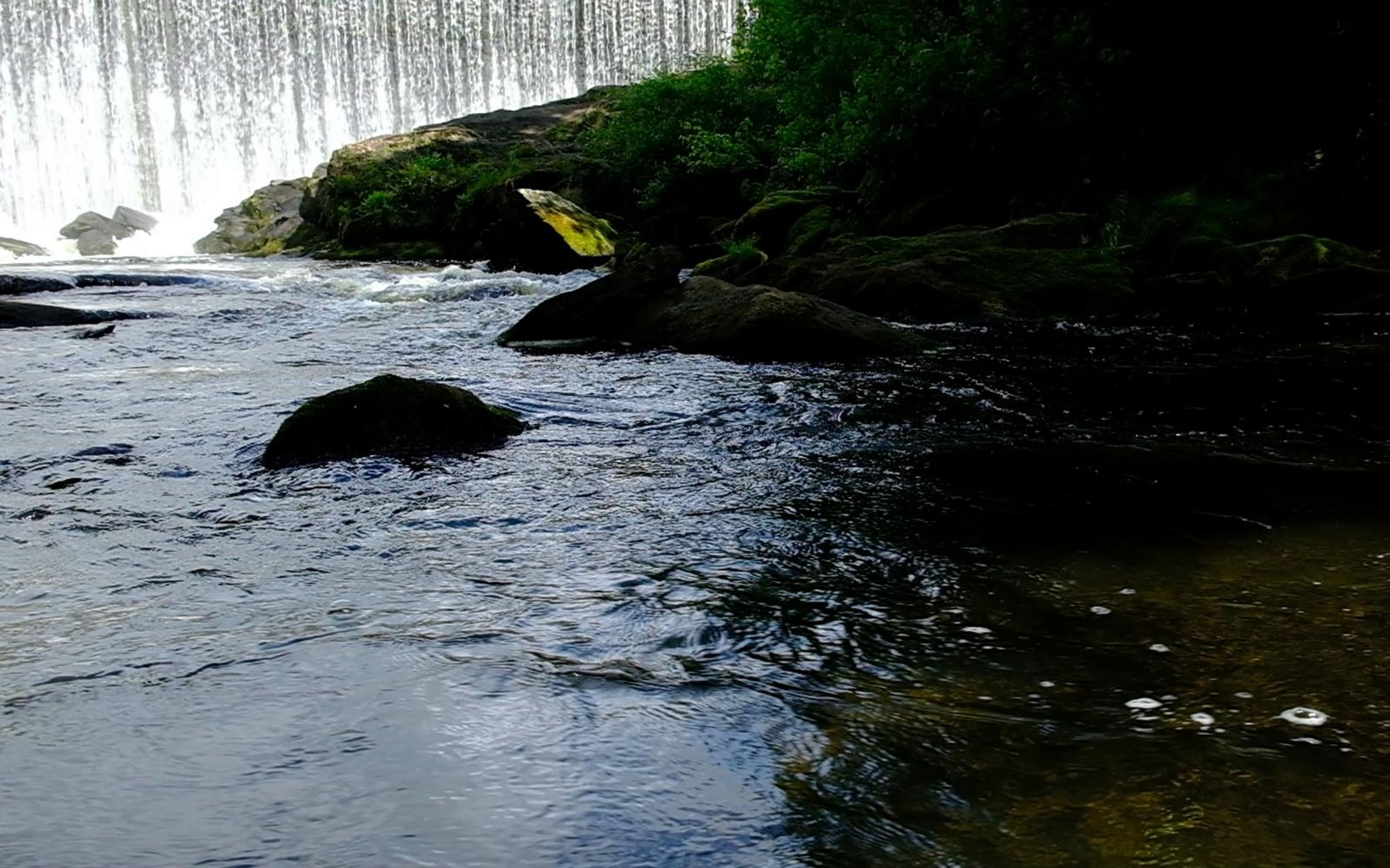 Wide river scene with a small rock in the water and the waterfall faintly visible beyond