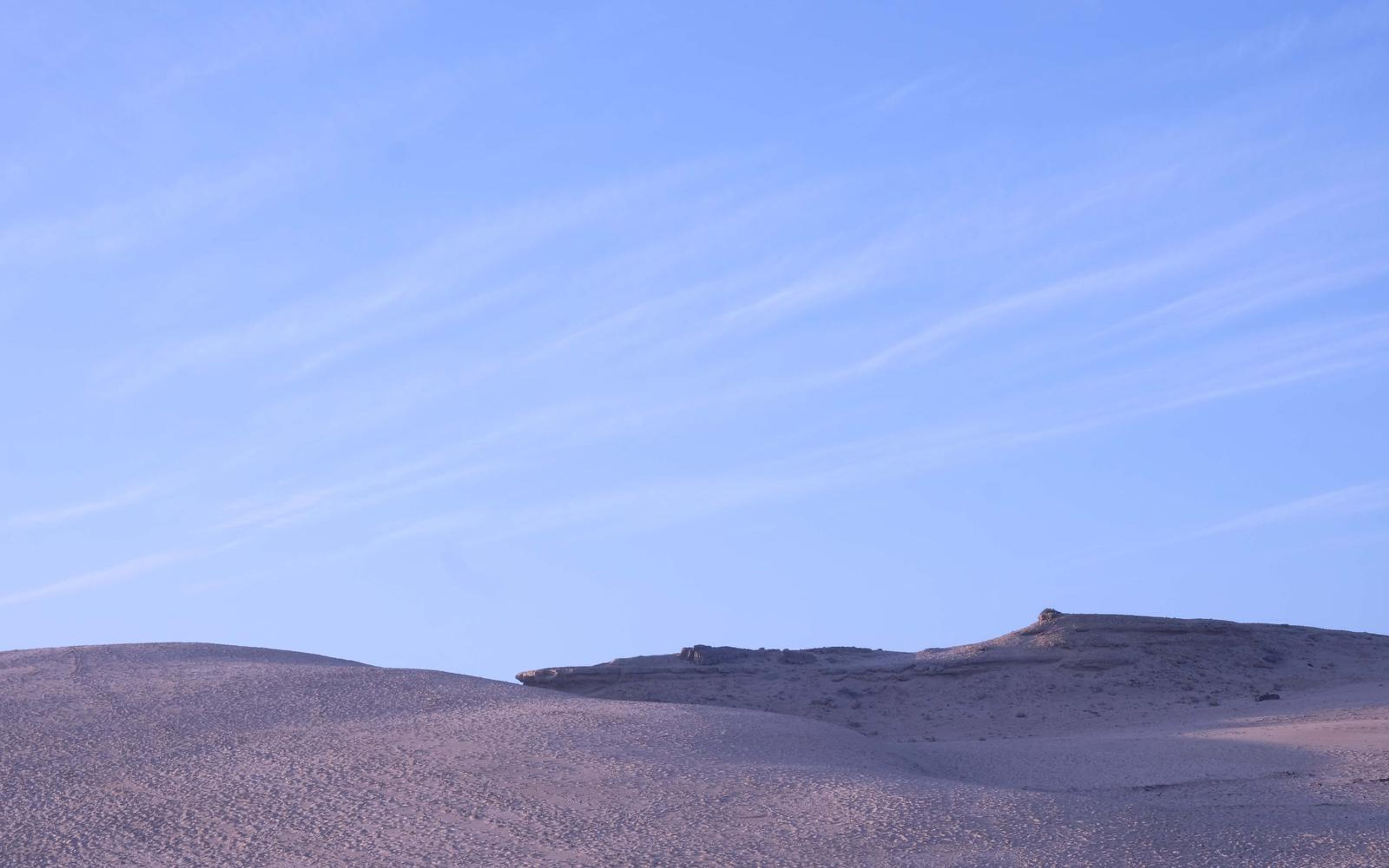 Smooth pale dune crest beneath a deep blue sky streaked with thin cloud