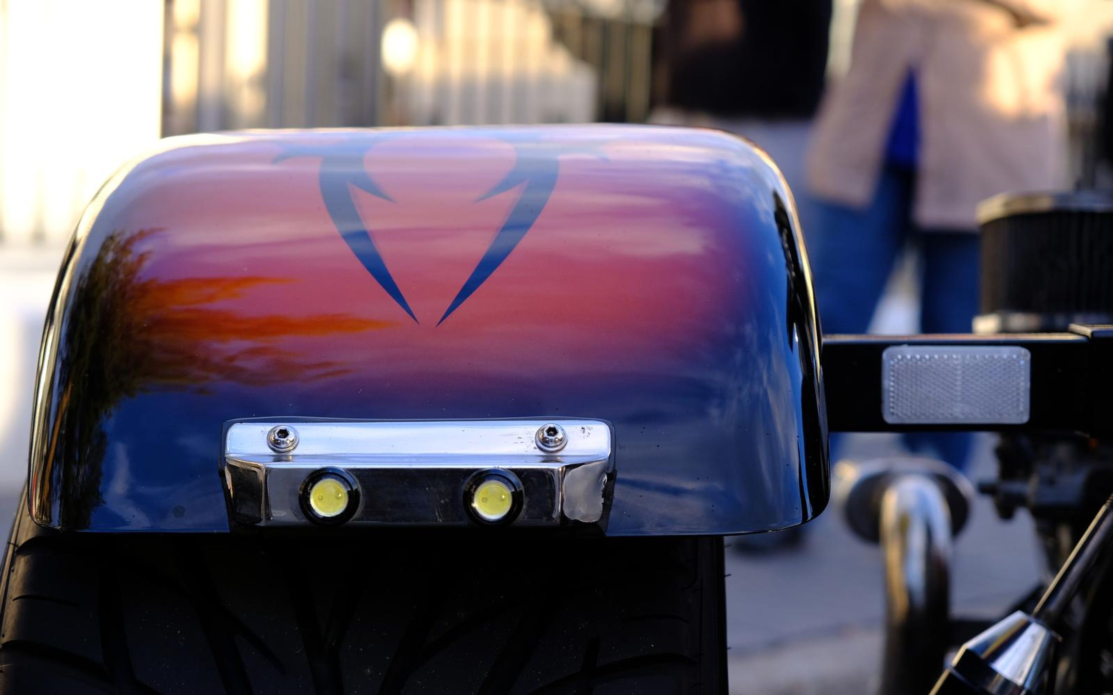 Close view of a rear fender painted with a blue to red fade and a dark wing shape, tyre tread below
